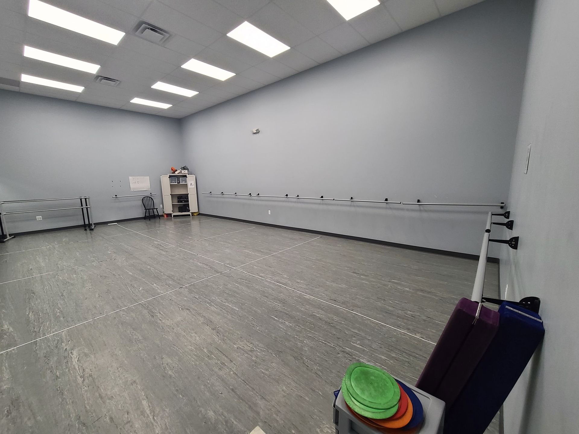 A large empty dance studio with a bunch of yoga mats on the floor.