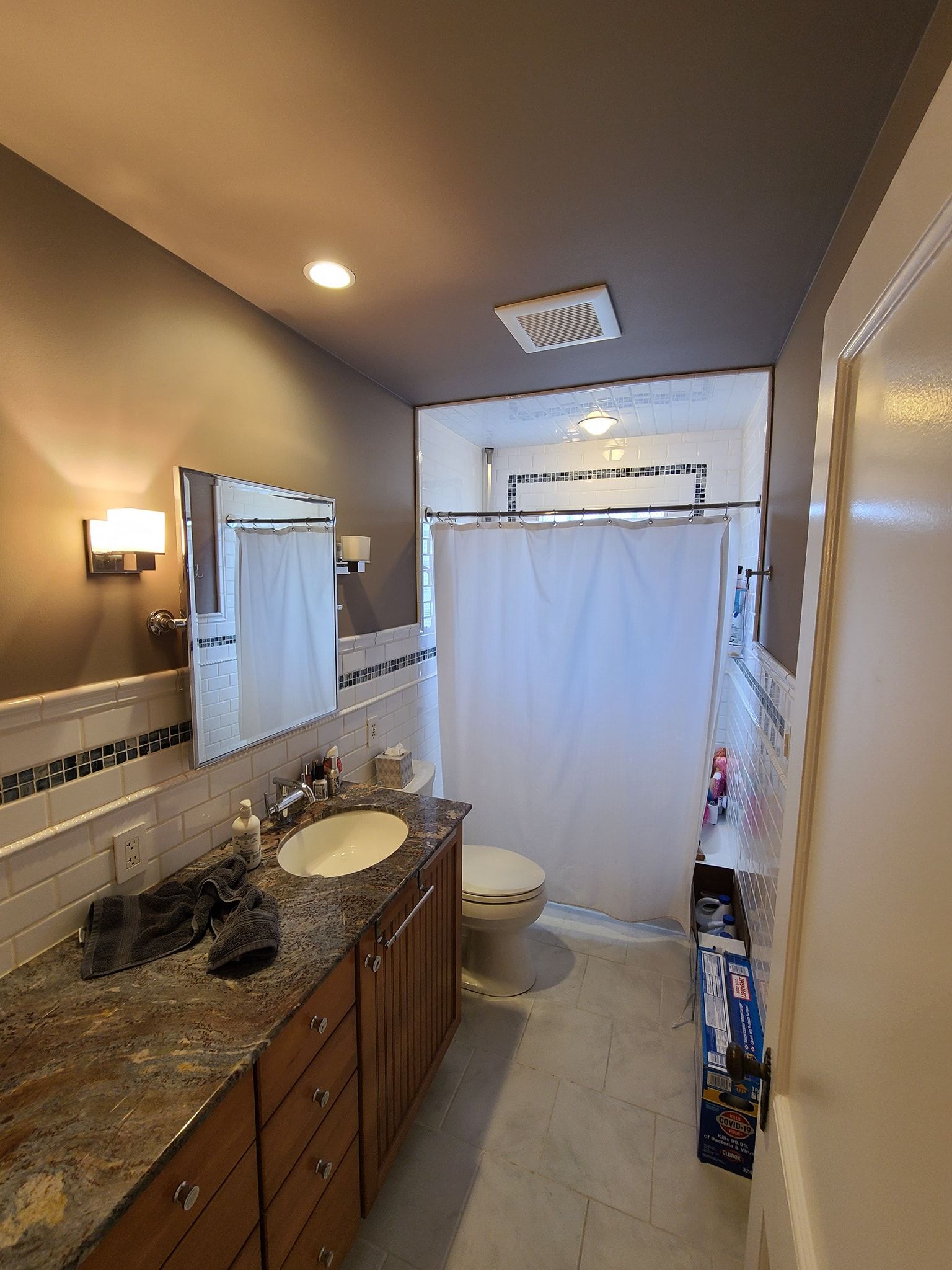 A bathroom with a toilet , sink , mirror and shower curtain.