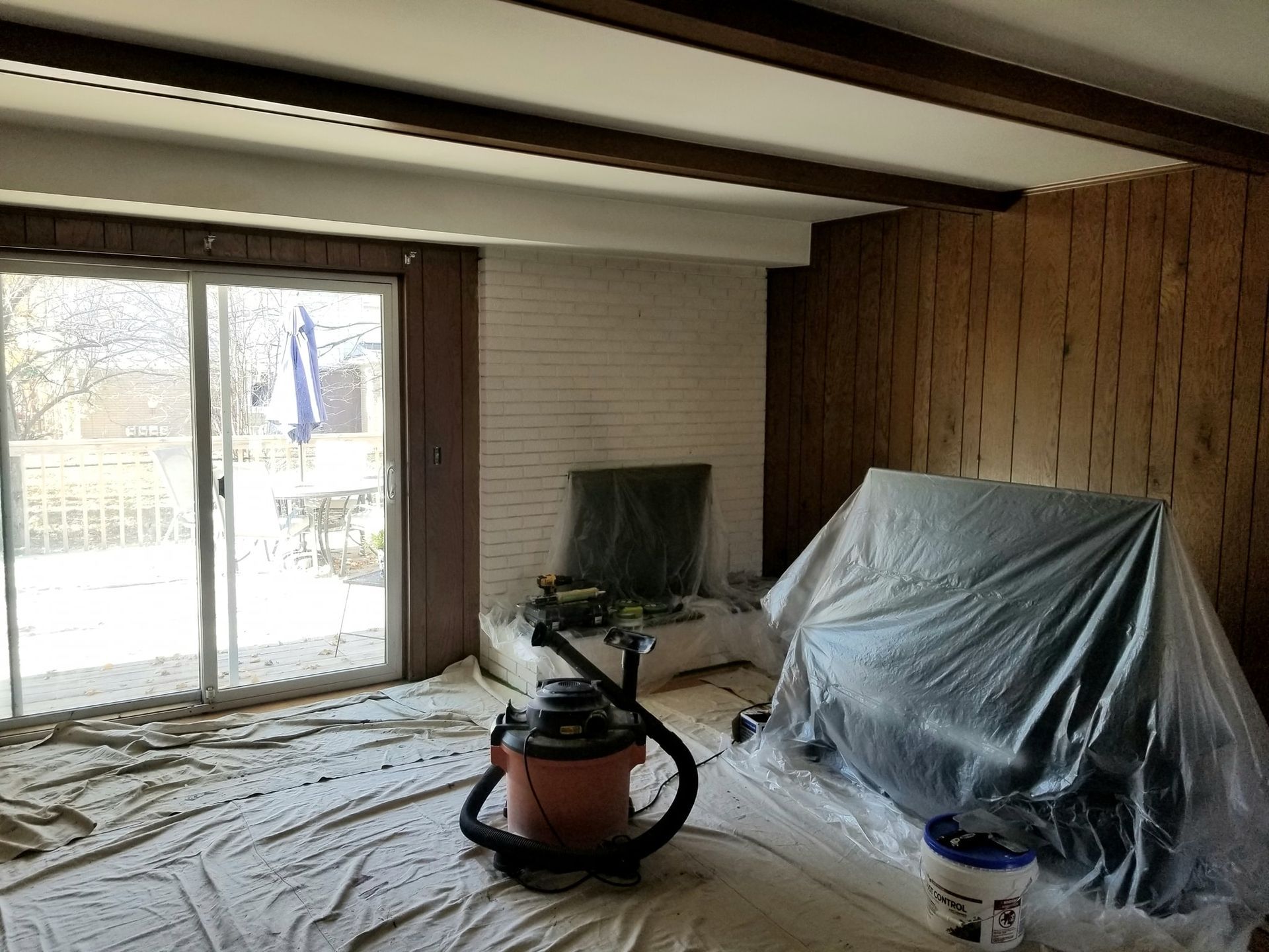 A living room with a vacuum cleaner and a couch covered in plastic.