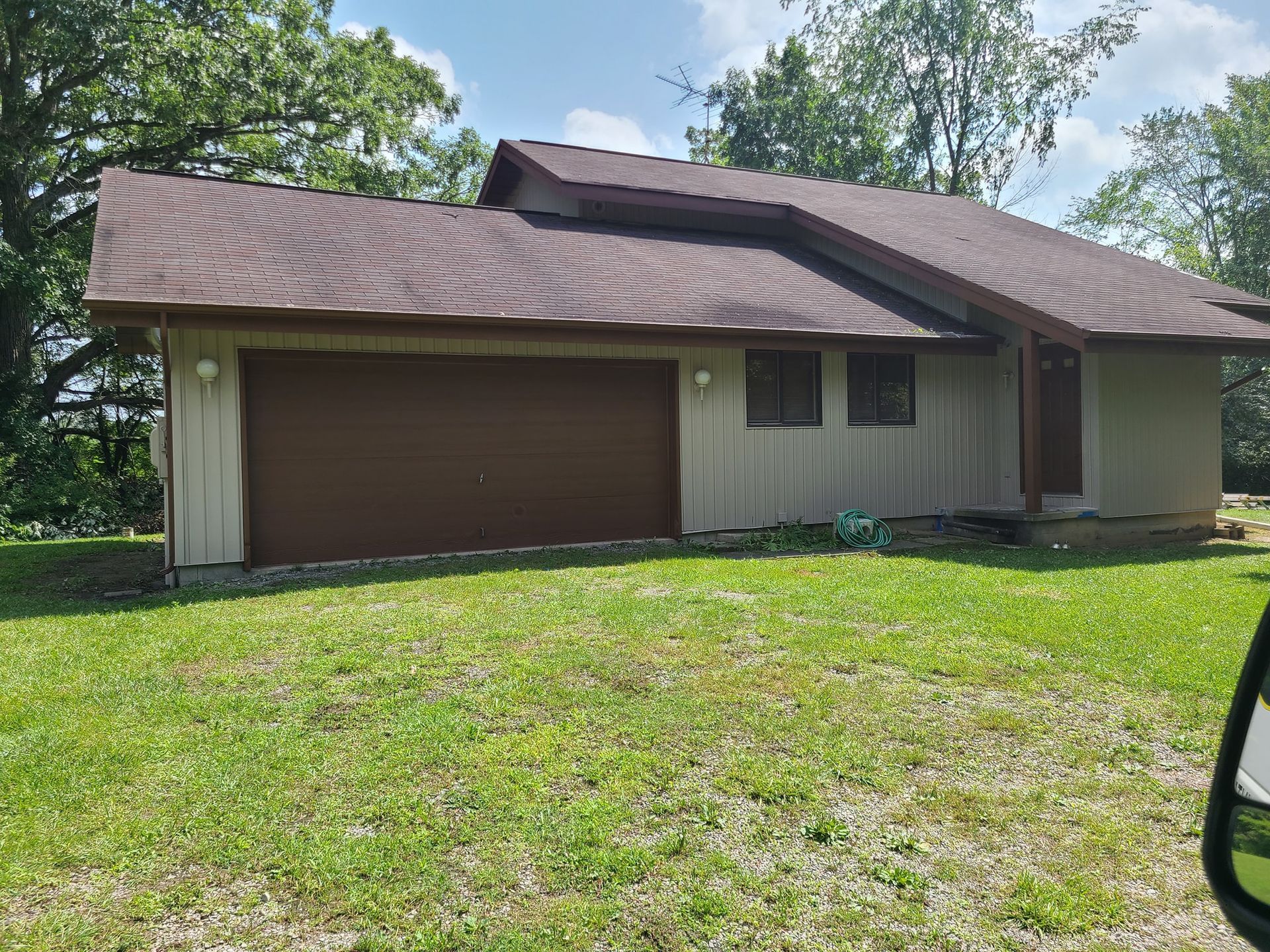A house with a brown garage door is sitting on top of a lush green field.