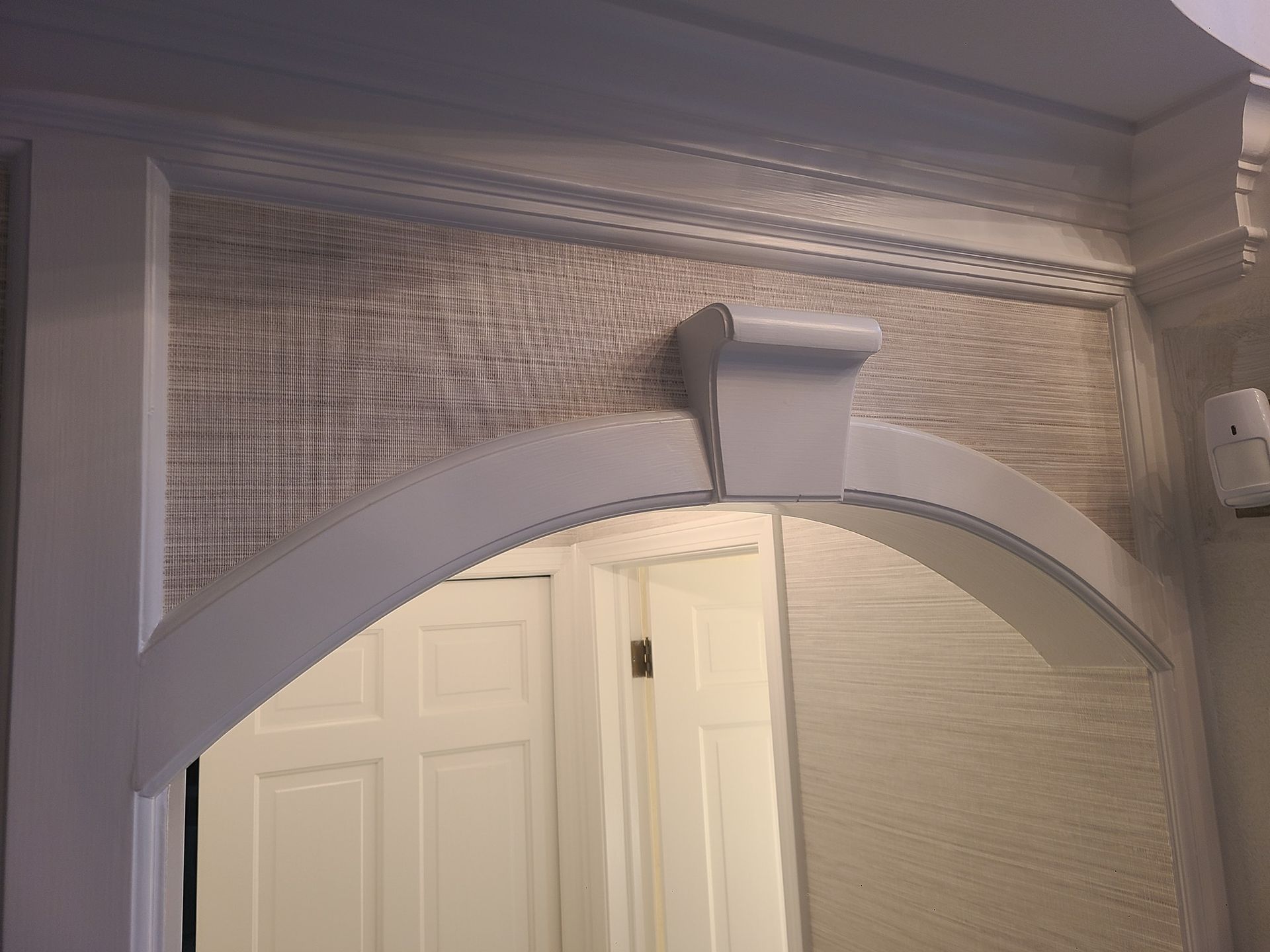 A white archway leading to a door in a room.