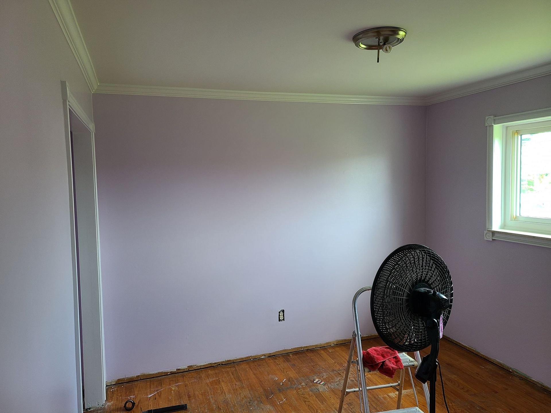 A room with purple walls and a fan on the floor.