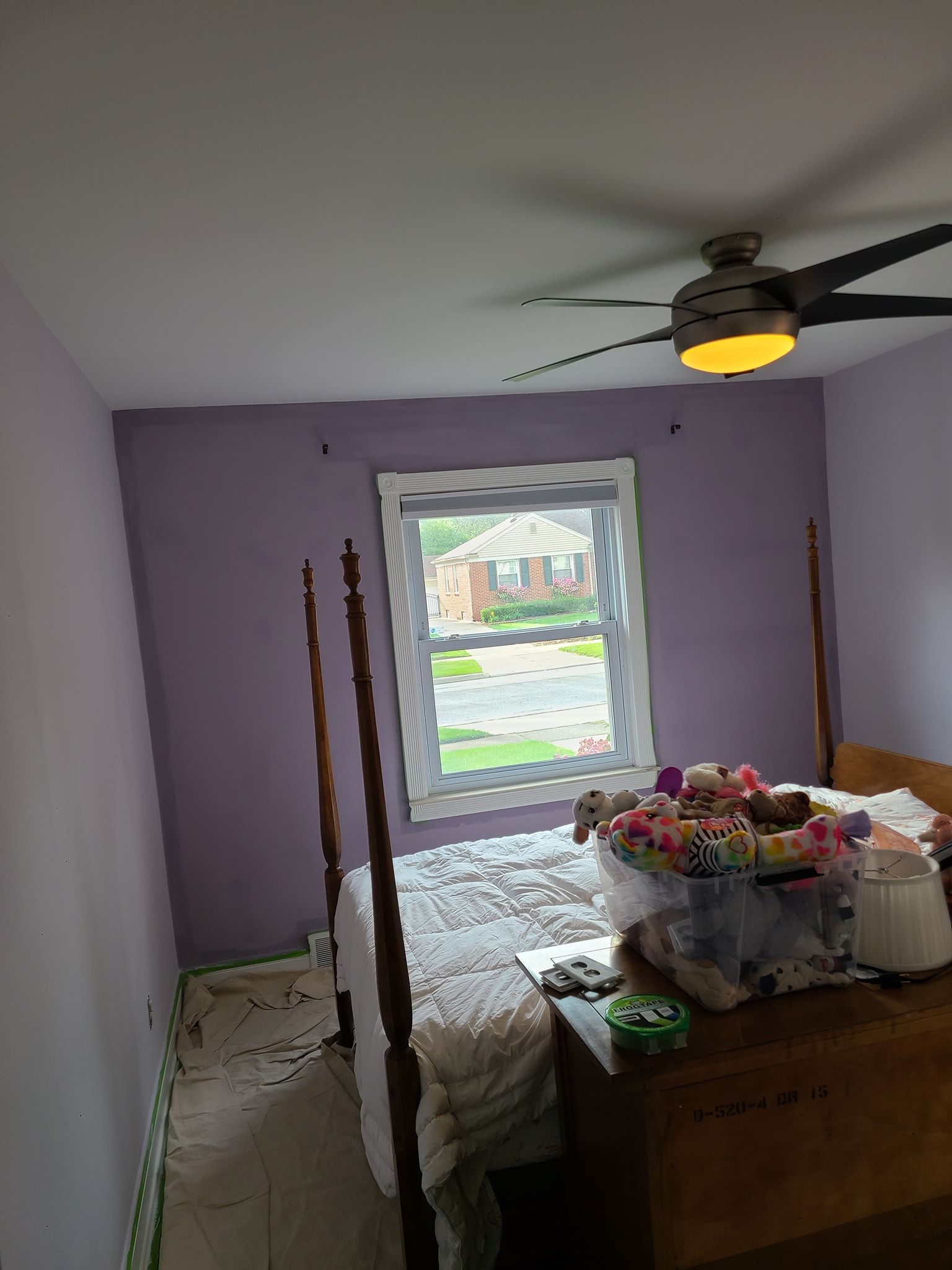 A bedroom with purple walls , a bed , a window and a ceiling fan.