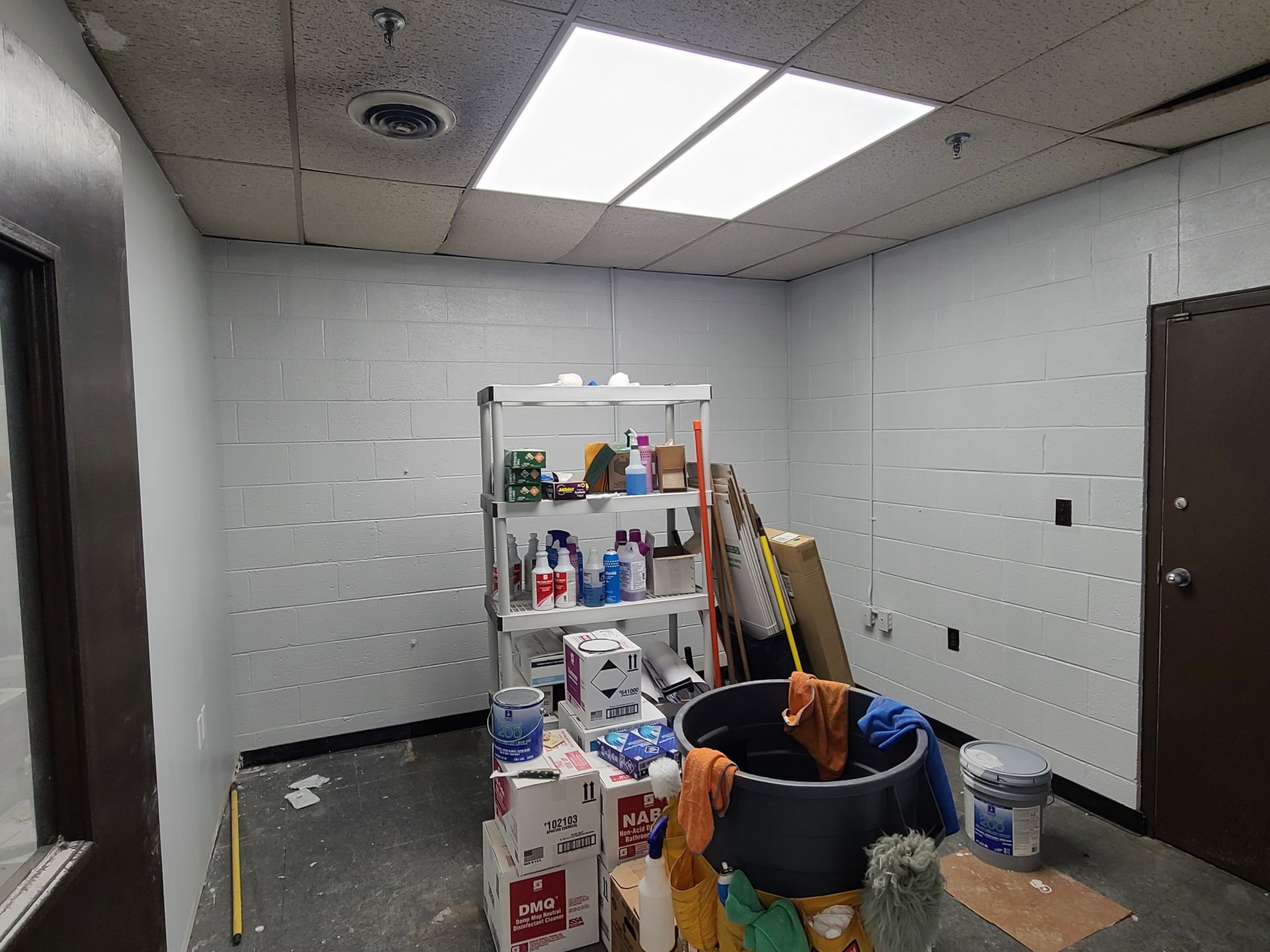 A room with a shelf full of cleaning supplies and a bucket on the floor.