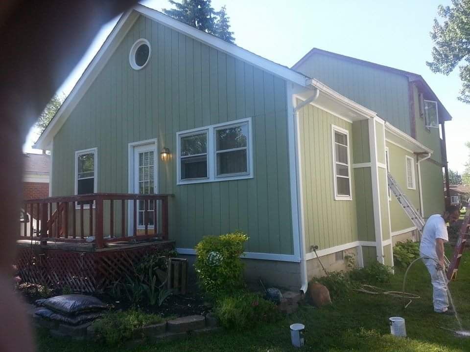 A man is painting the side of a green house
