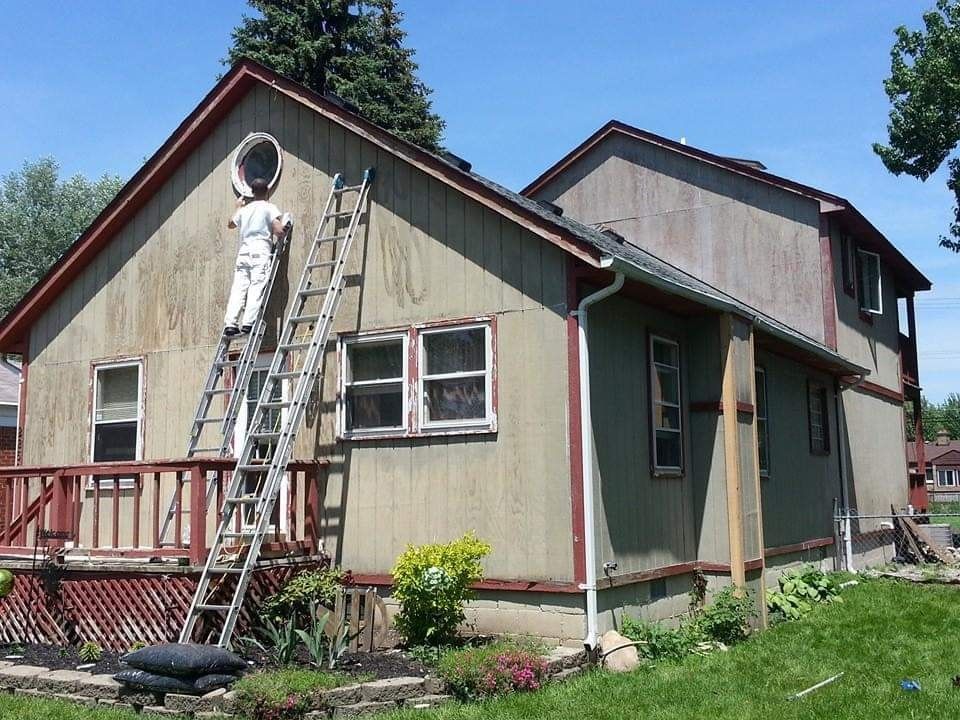 A man on a ladder paints the side of a house
