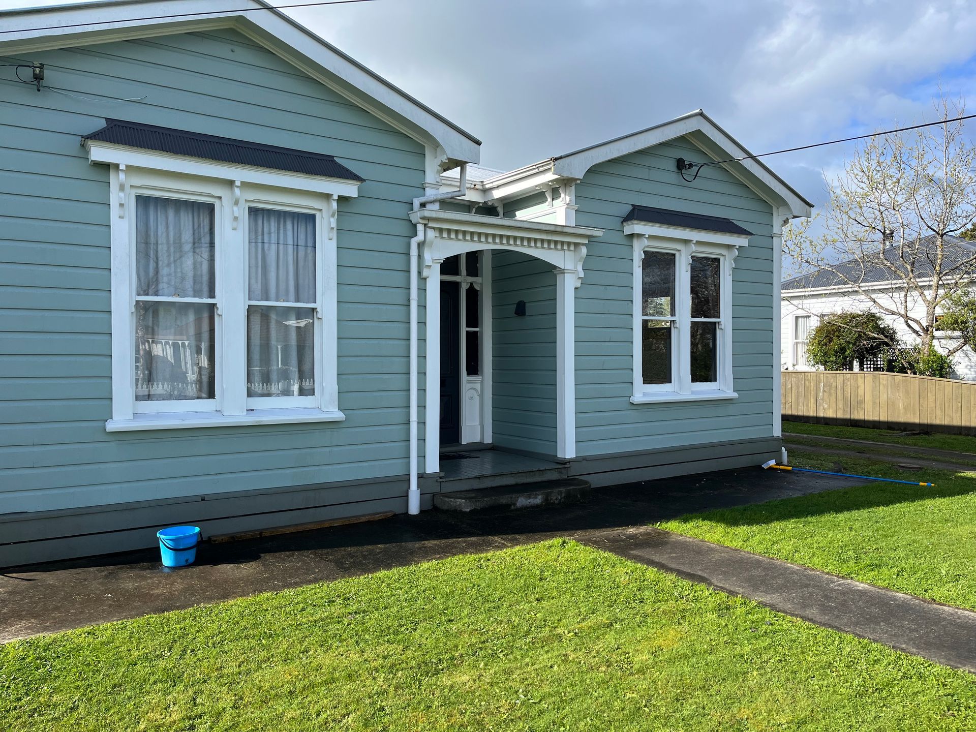 A blue house with white windows and a blue bucket in front of it.