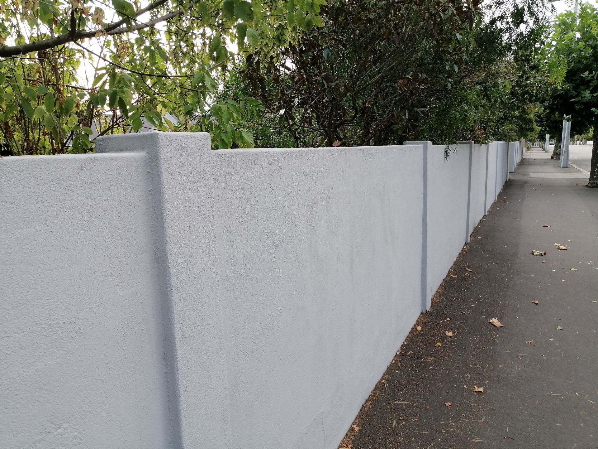 A white fence along a sidewalk with trees in the background