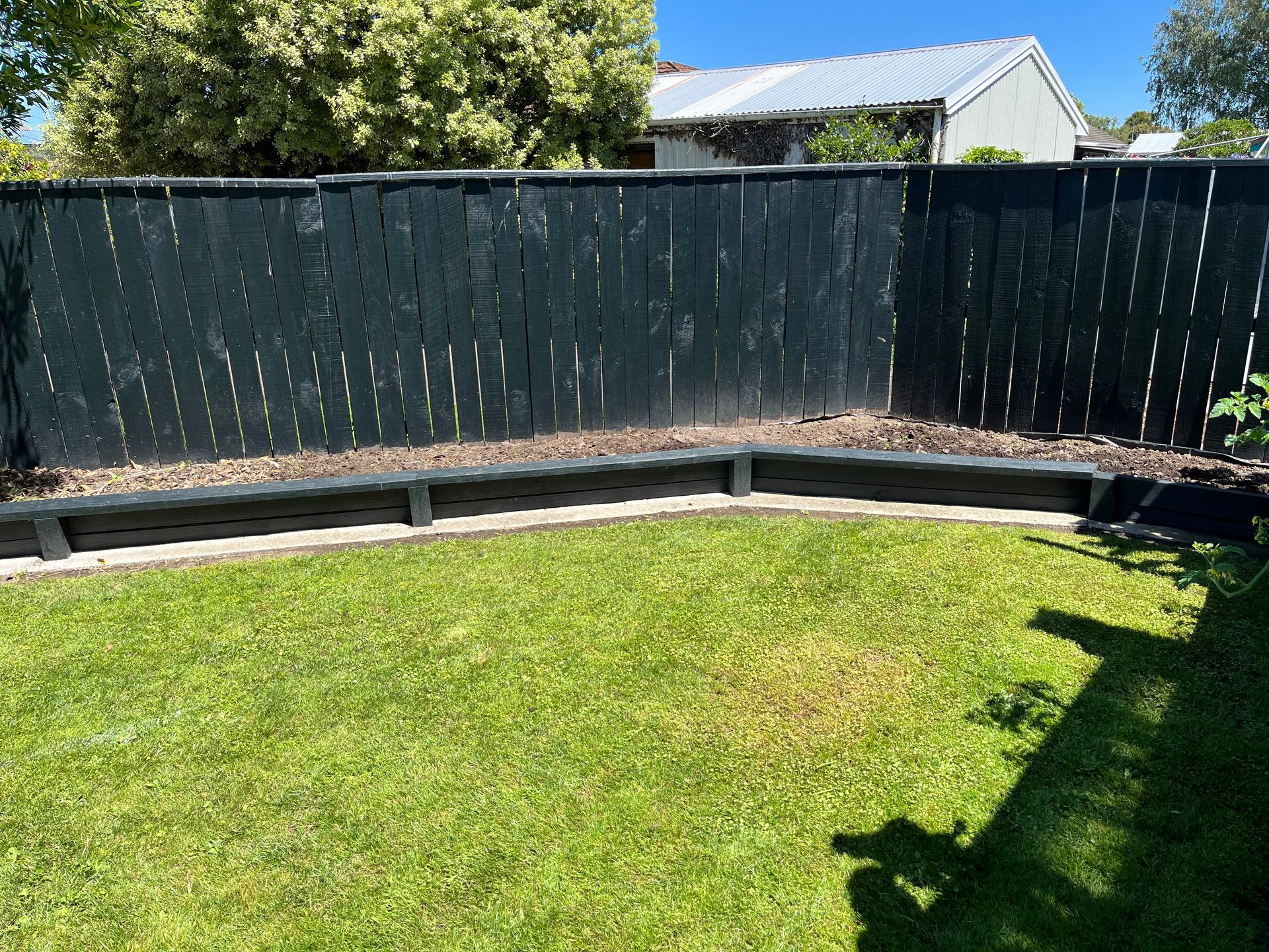 A black fence surrounds a lush green lawn in a backyard.