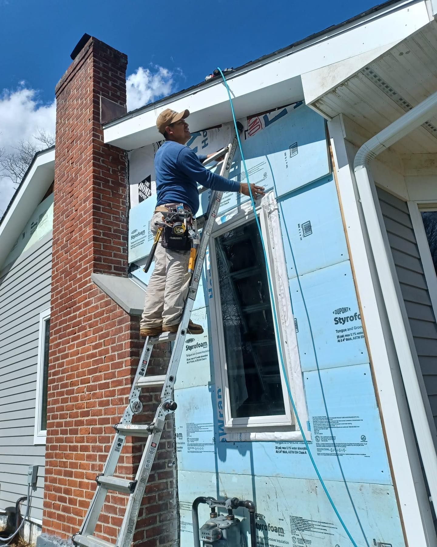A man is standing on a ladder on the side of a house.