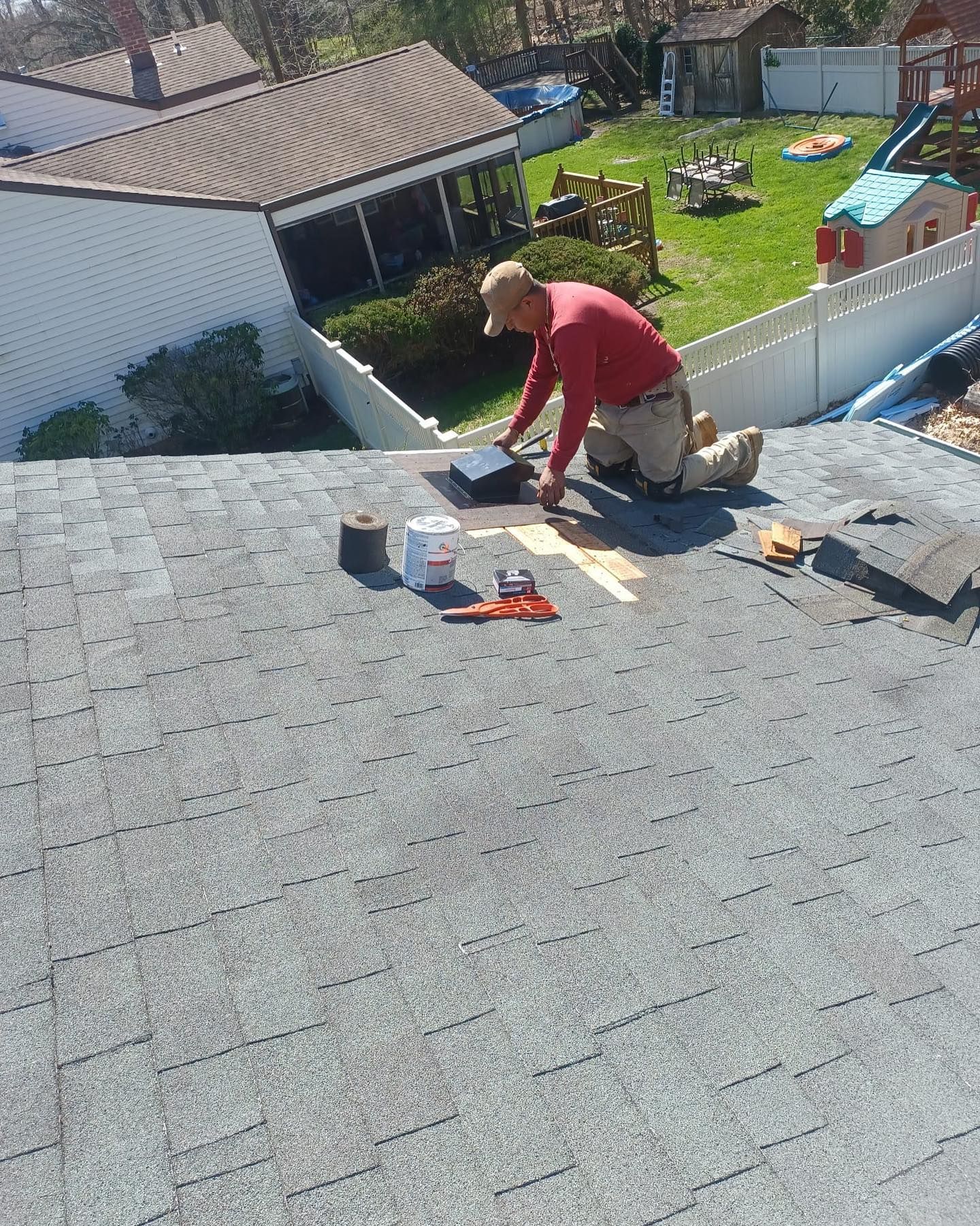 A man is kneeling on top of a roof working on it.