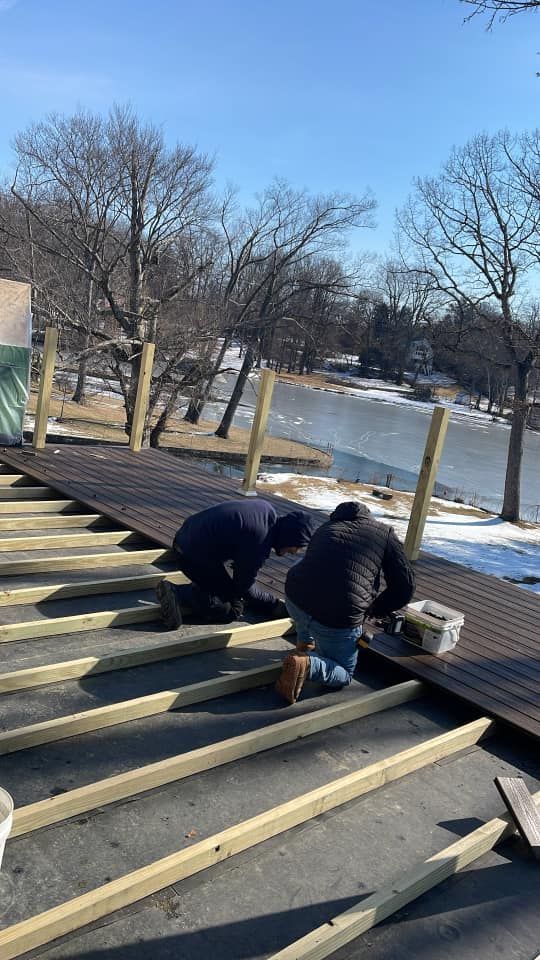 Two men are working on a wooden deck next to a lake.