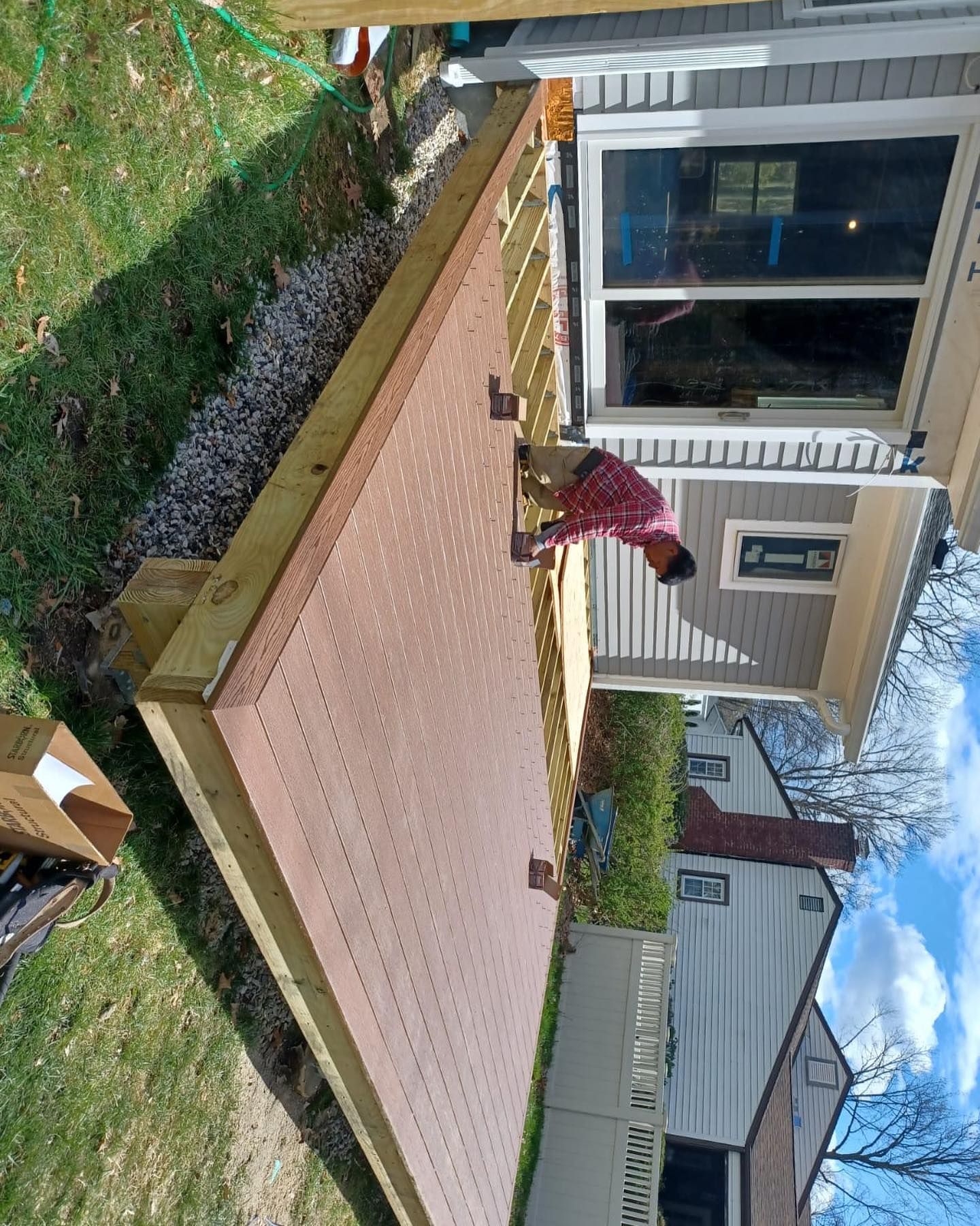 A man is working on a wooden deck in front of a house.