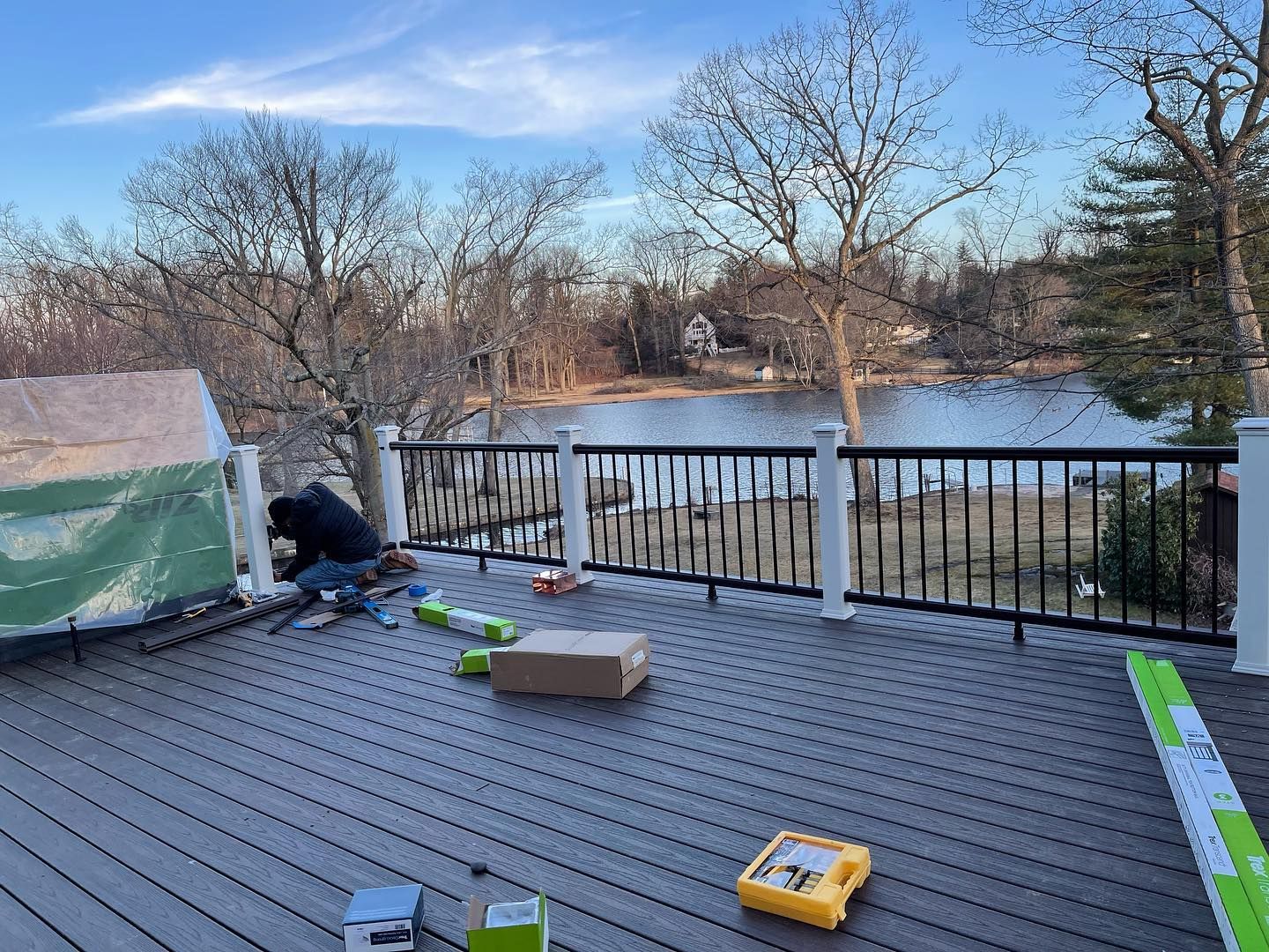 A man is working on a deck overlooking a lake.