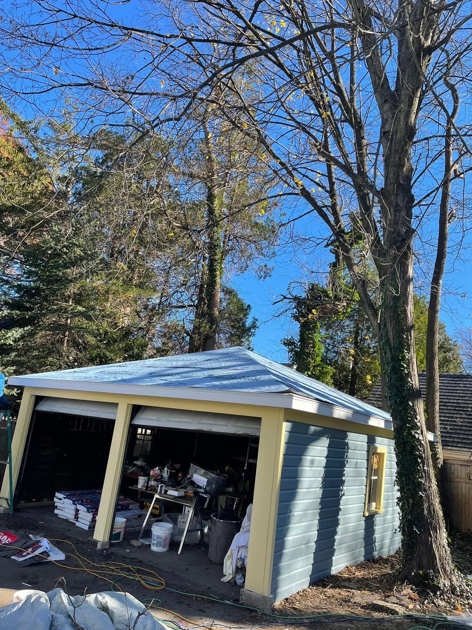 A blue garage with a white roof is surrounded by trees on a sunny day.