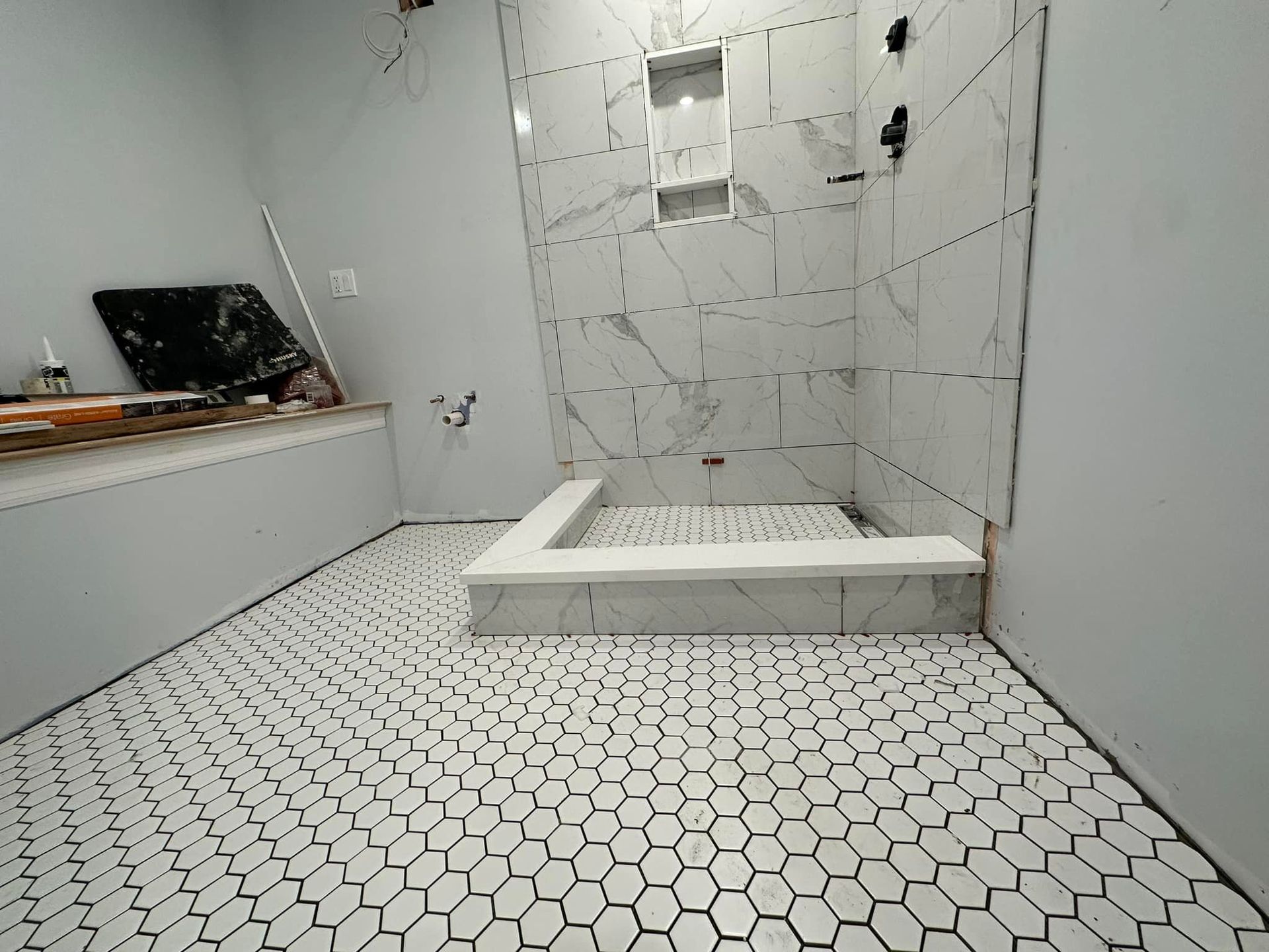 A bathroom with white tiles and a shower stall under construction.