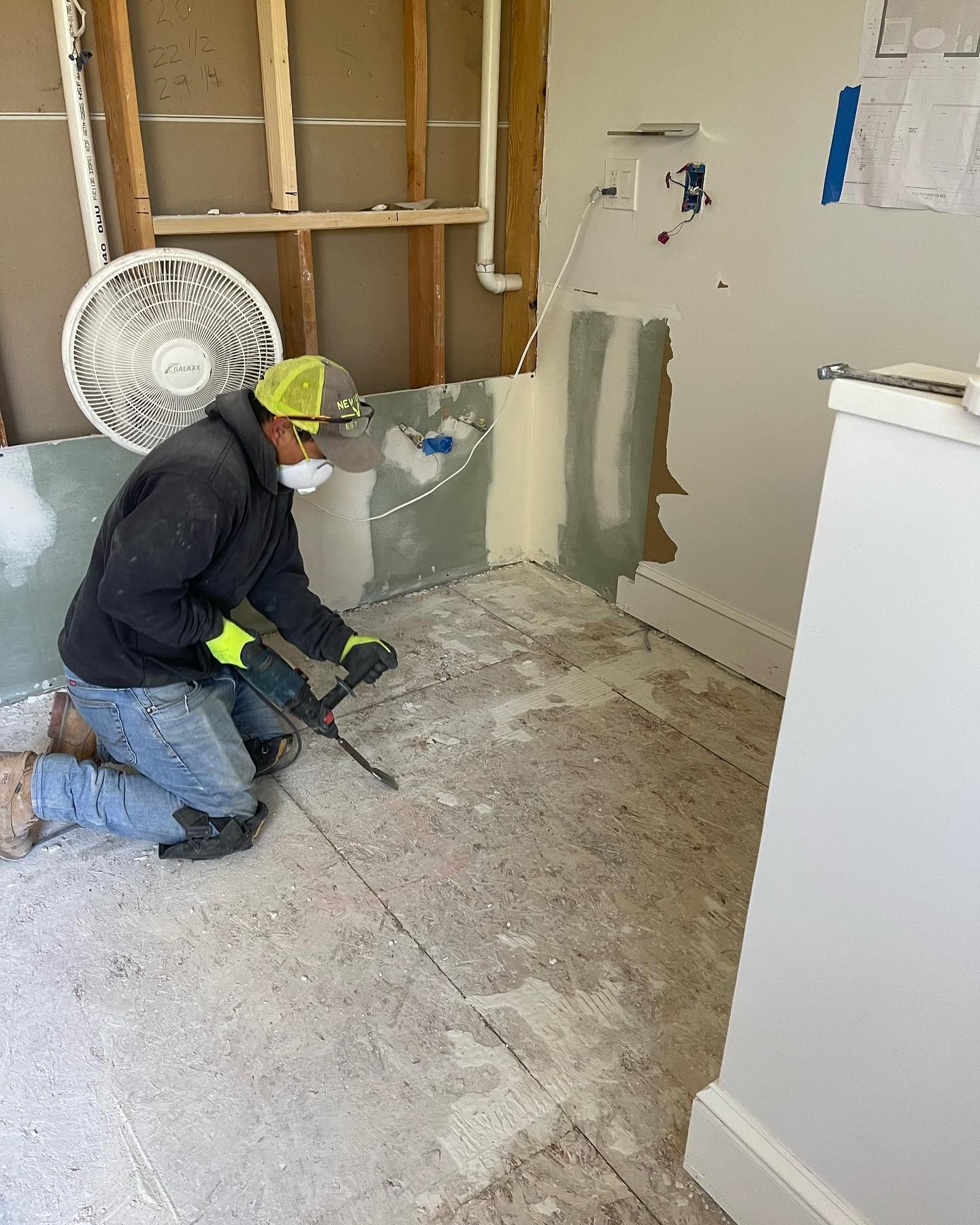 A man is kneeling down in a room holding a hammer.