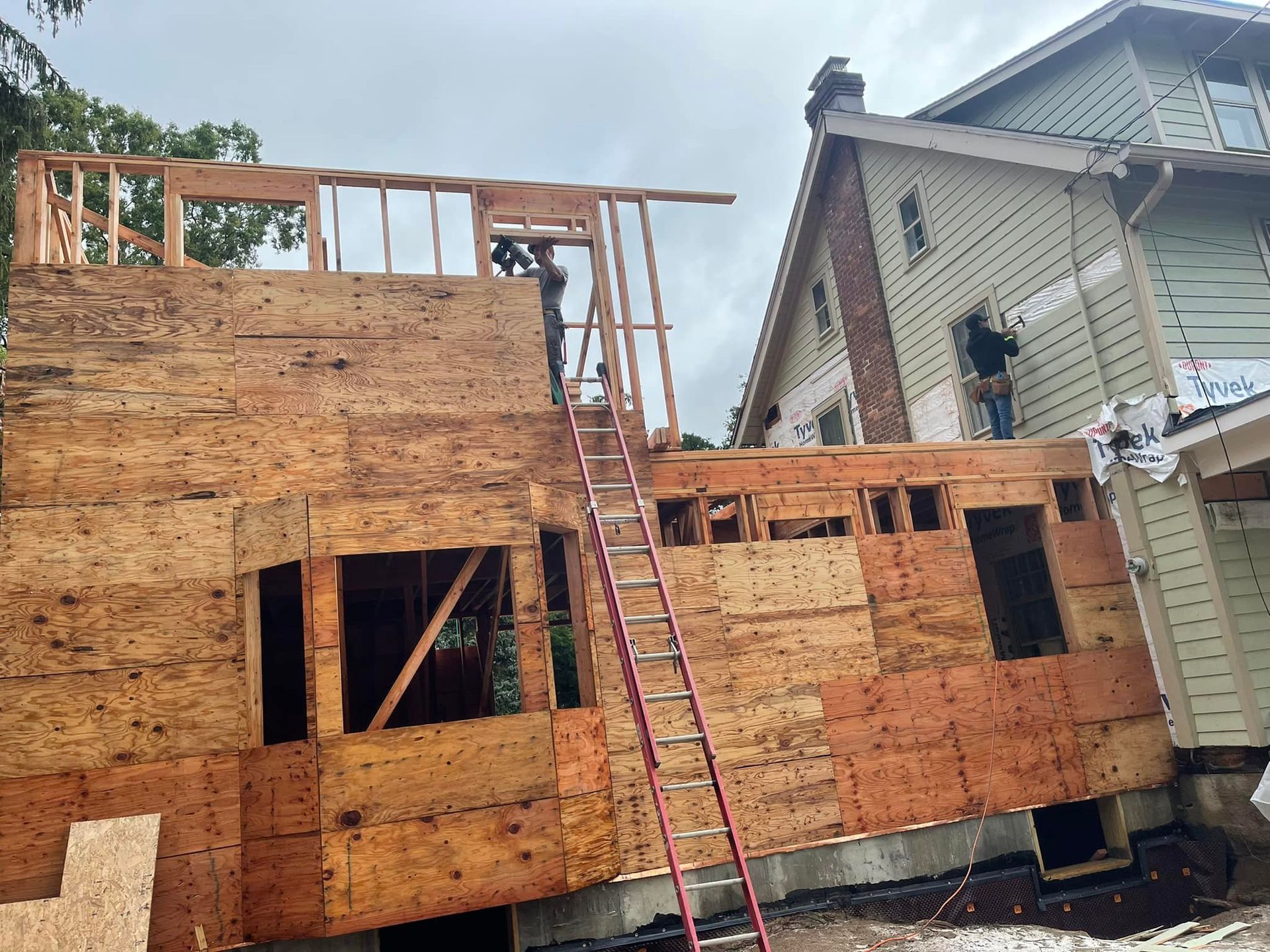 A wooden house is being built with a ladder in front of it.