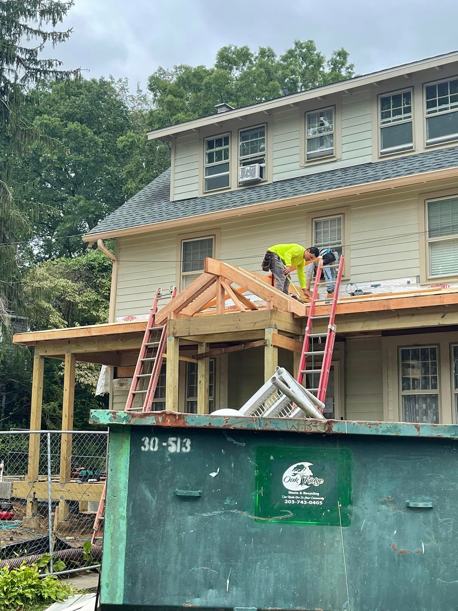 A man is working on the roof of a house next to a dumpster.