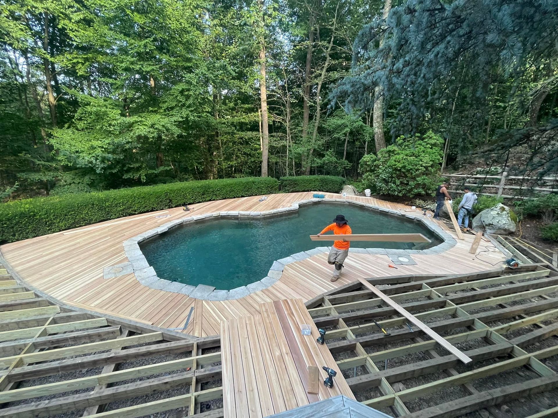 A man is standing on a wooden deck next to a swimming pool.
