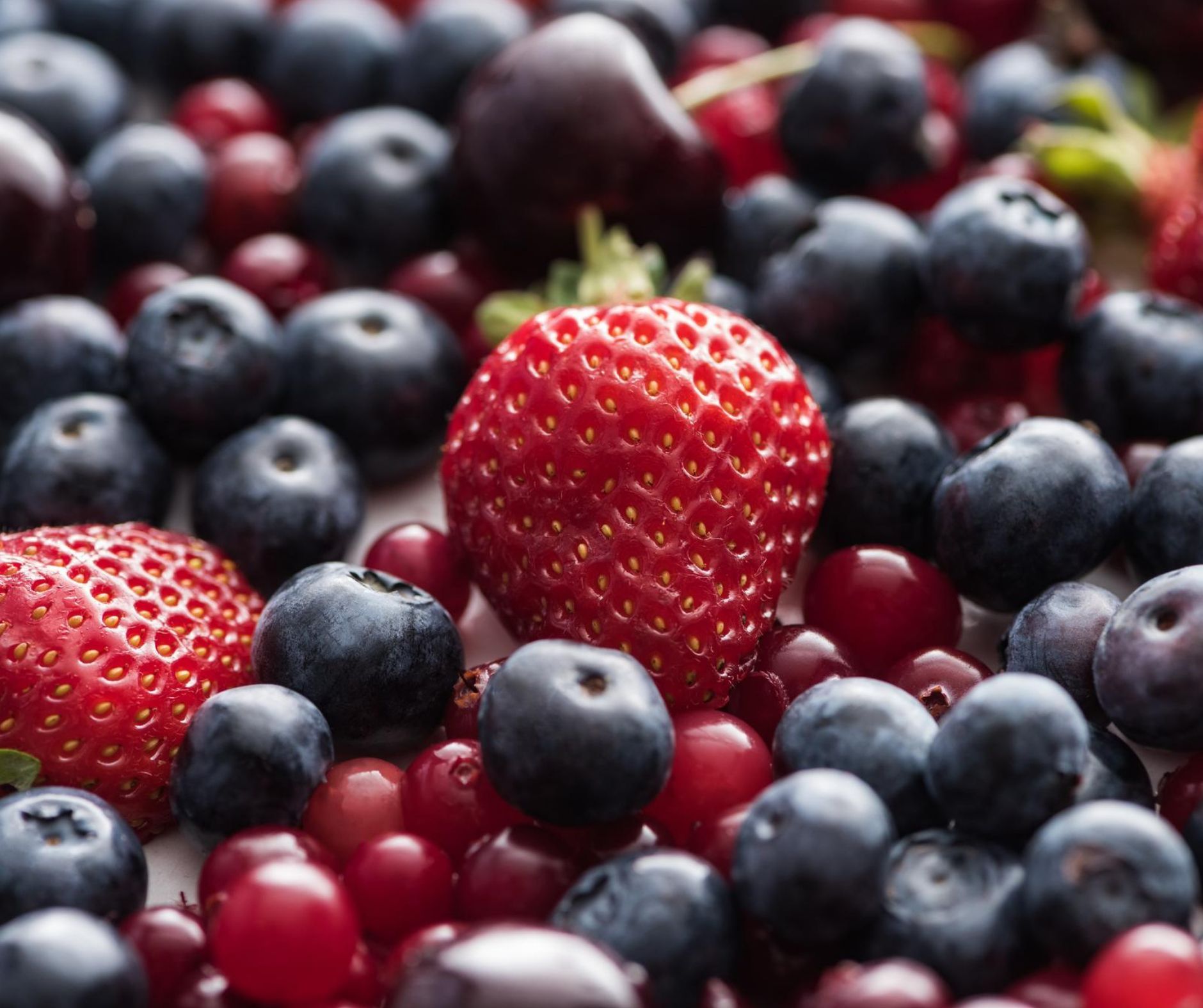 A strawberry is surrounded by blueberries and cranberries
