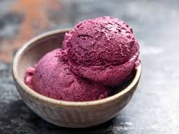 Two scoops of purple ice cream in a bowl on a table.