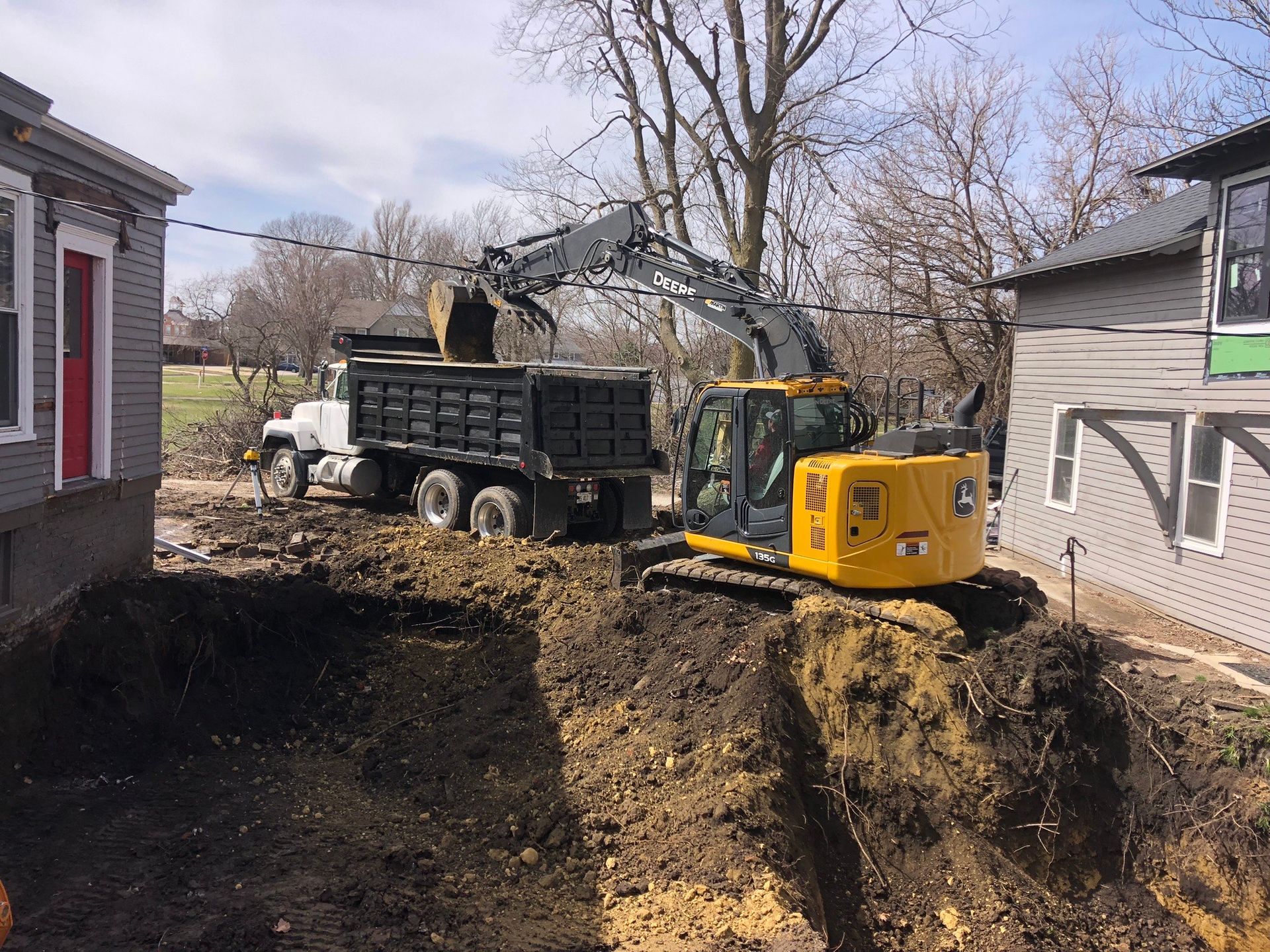 A yellow excavator is loading dirt into a dump truck. -  Elpaso, IL - LT Excavating