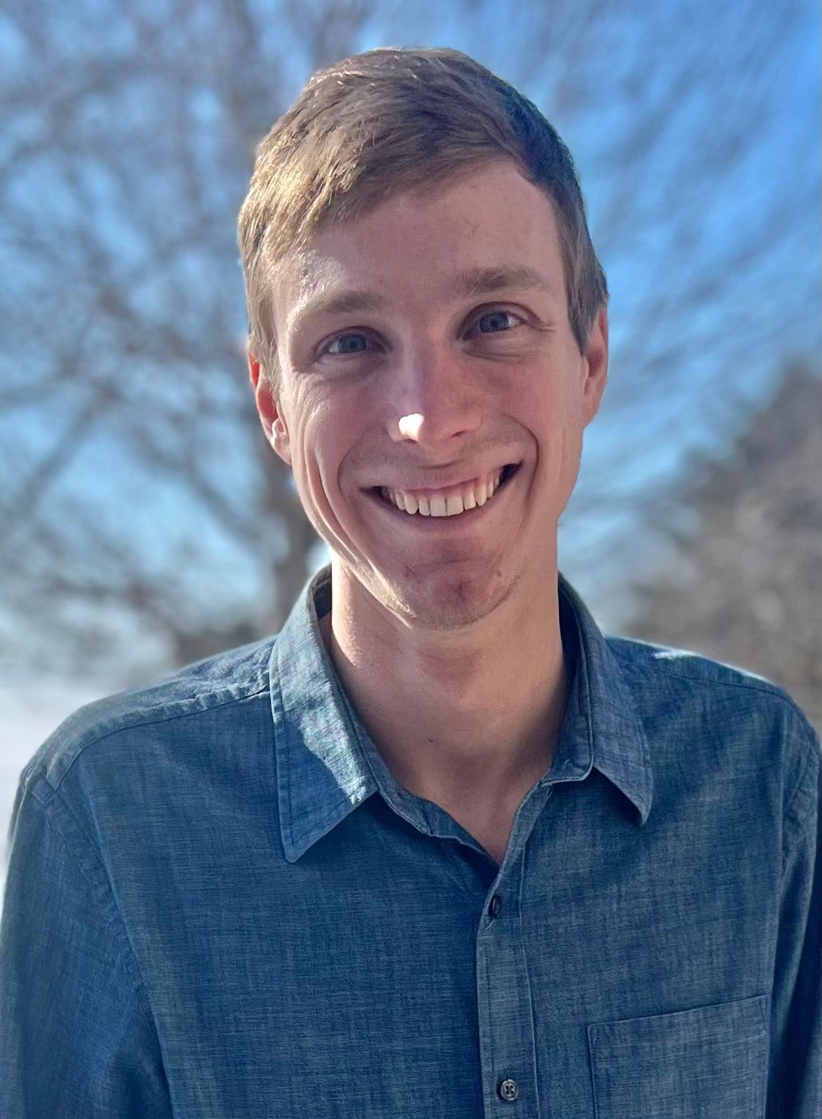 A young man in a blue shirt is smiling for the camera.