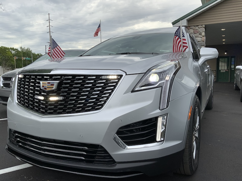 Silver Cadillac SUV with American flags attached to the front; parked outdoors.