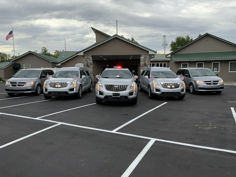 Five silver SUVs and vans parked in front of a tan building under a cloudy sky.