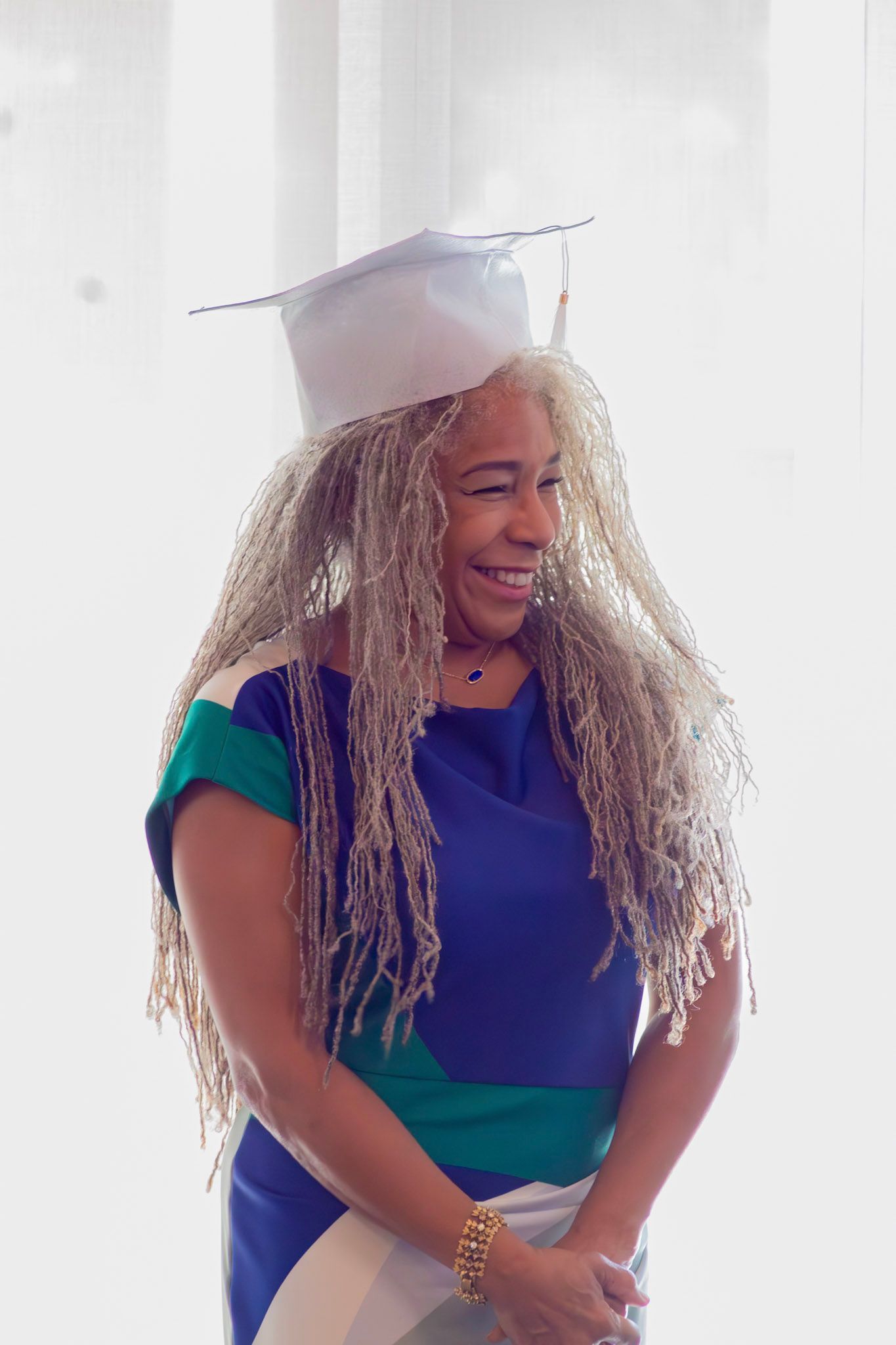 Person wearing graduation cap, smiling, in blue, green, and white dress.