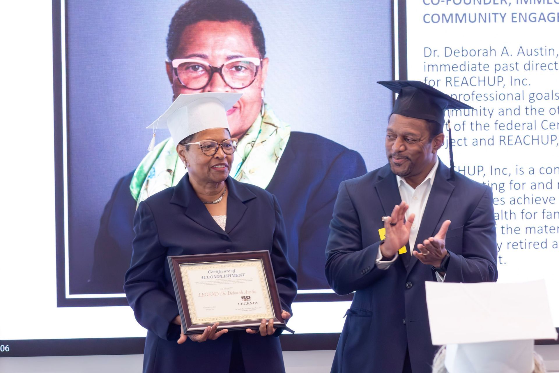 Woman in cap and gown holds a certificate, man claps; a screen shows a photo of the woman.