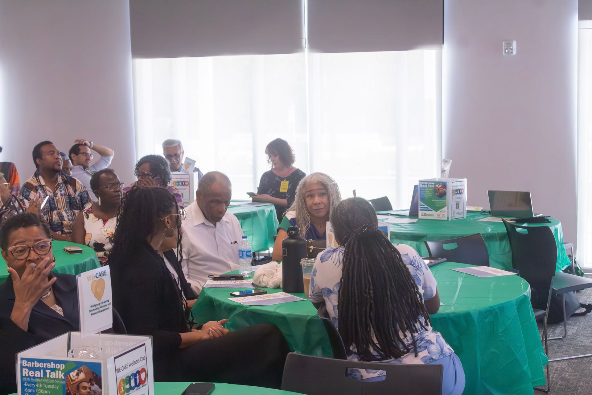 People seated at tables in a room, some looking up. Tables are covered in green cloths.