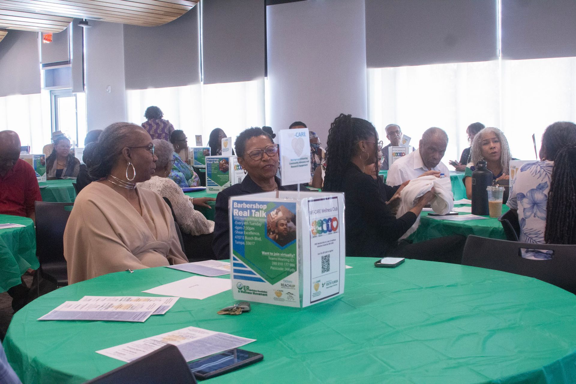 People seated at tables covered in green tablecloths in a large room.
