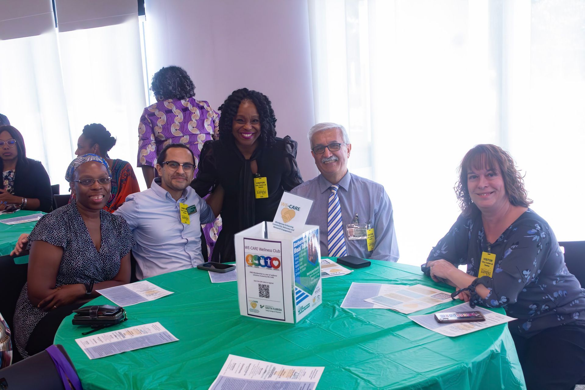 People seated at a table covered in green fabric, smiling and looking at the camera; an event.