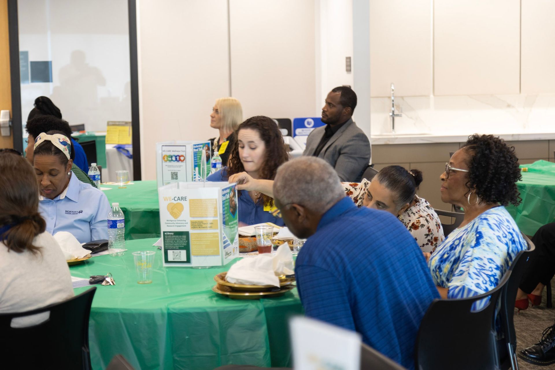 People seated around a table covered in green cloth. Several are eating or looking at food.