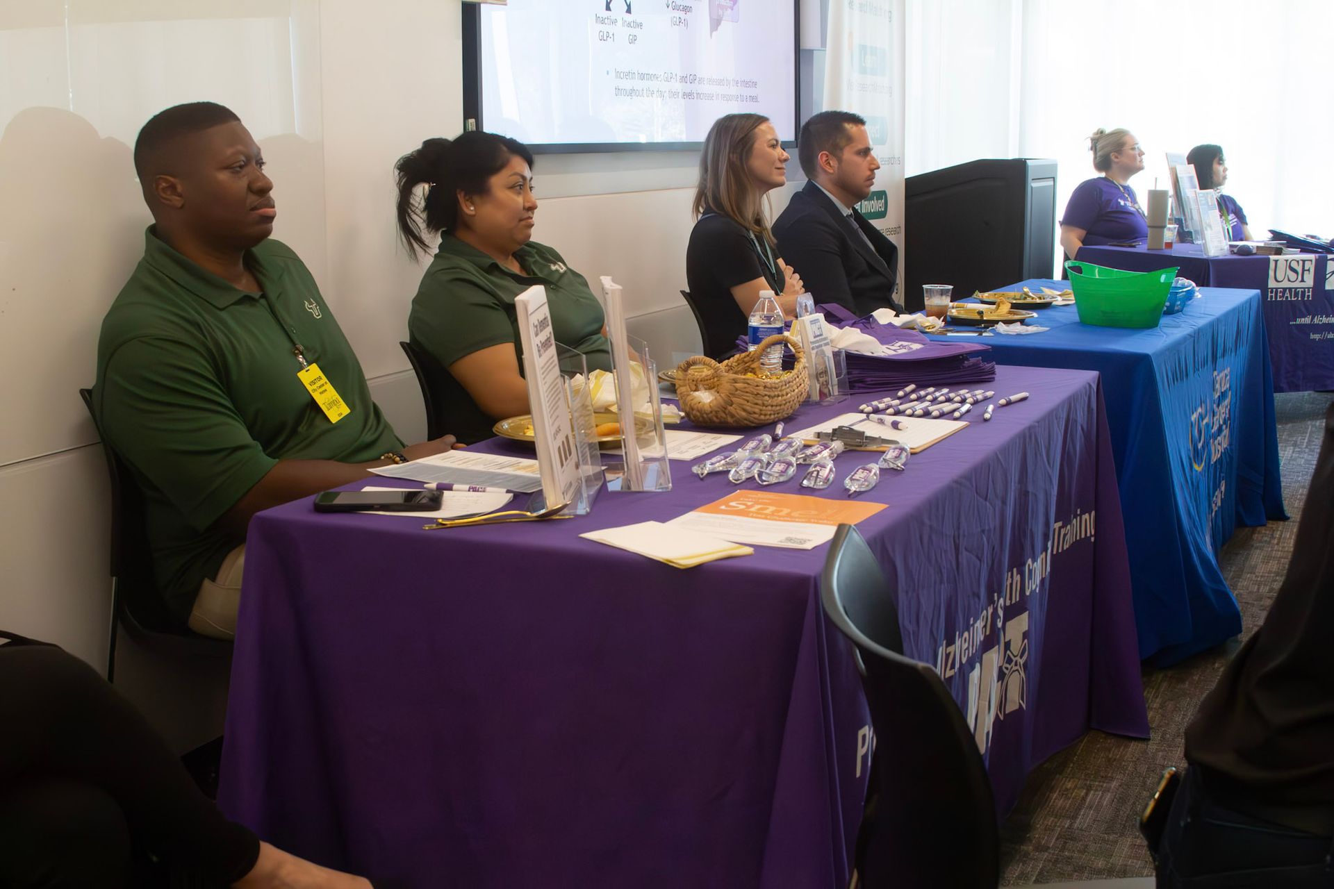 People seated at tables with purple tablecloths, some wearing name tags and looking forward.
