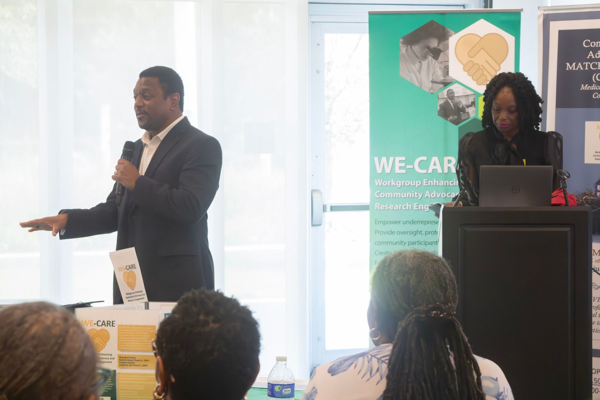 Man speaking at a lectern, woman at a laptop, a 