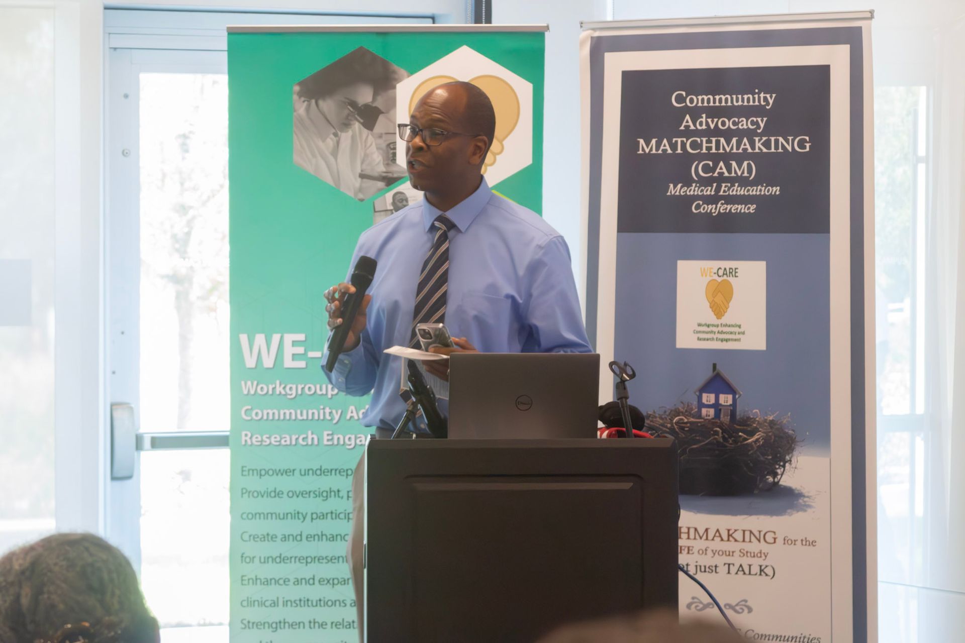 Man speaking at podium with banners behind him, inside a room.