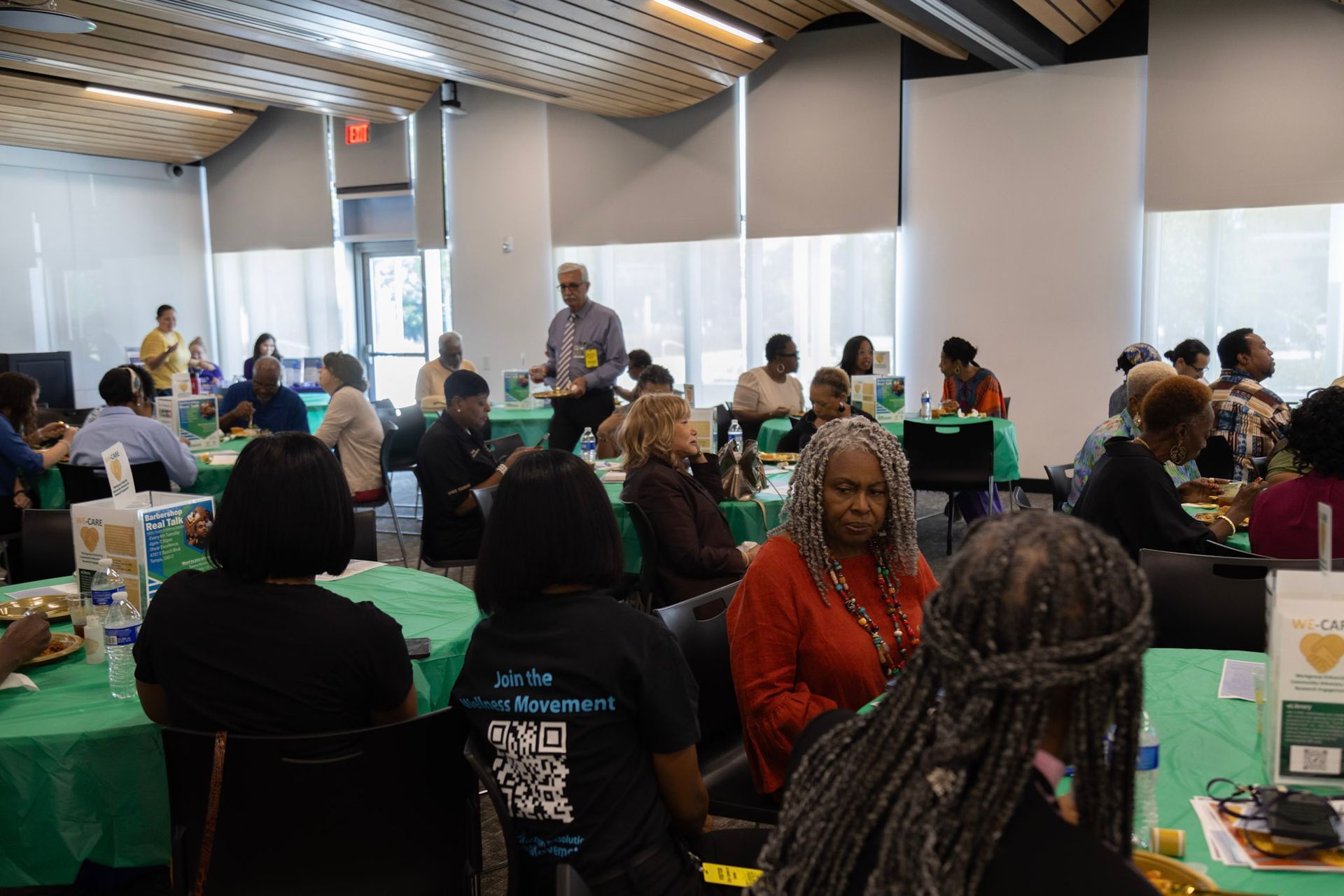 A conference or meeting with attendees seated at tables with green tablecloths. A man walks in the aisle.