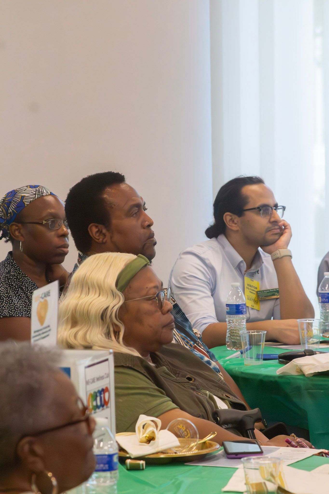 Attendees seated at a table, listening attentively. Individuals are looking towards the same direction.