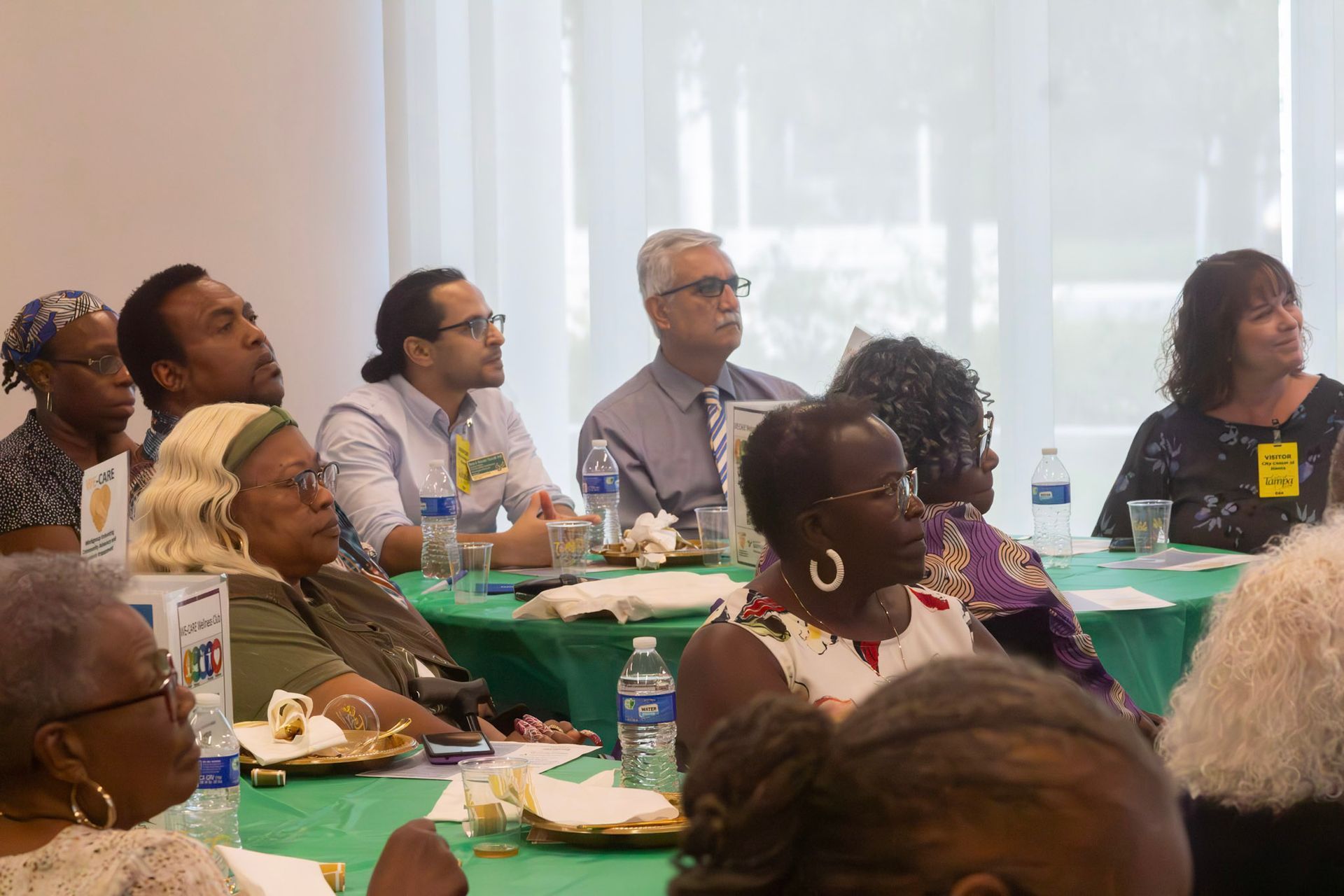 People seated around a green table, looking toward the same direction. They are in a well-lit room.