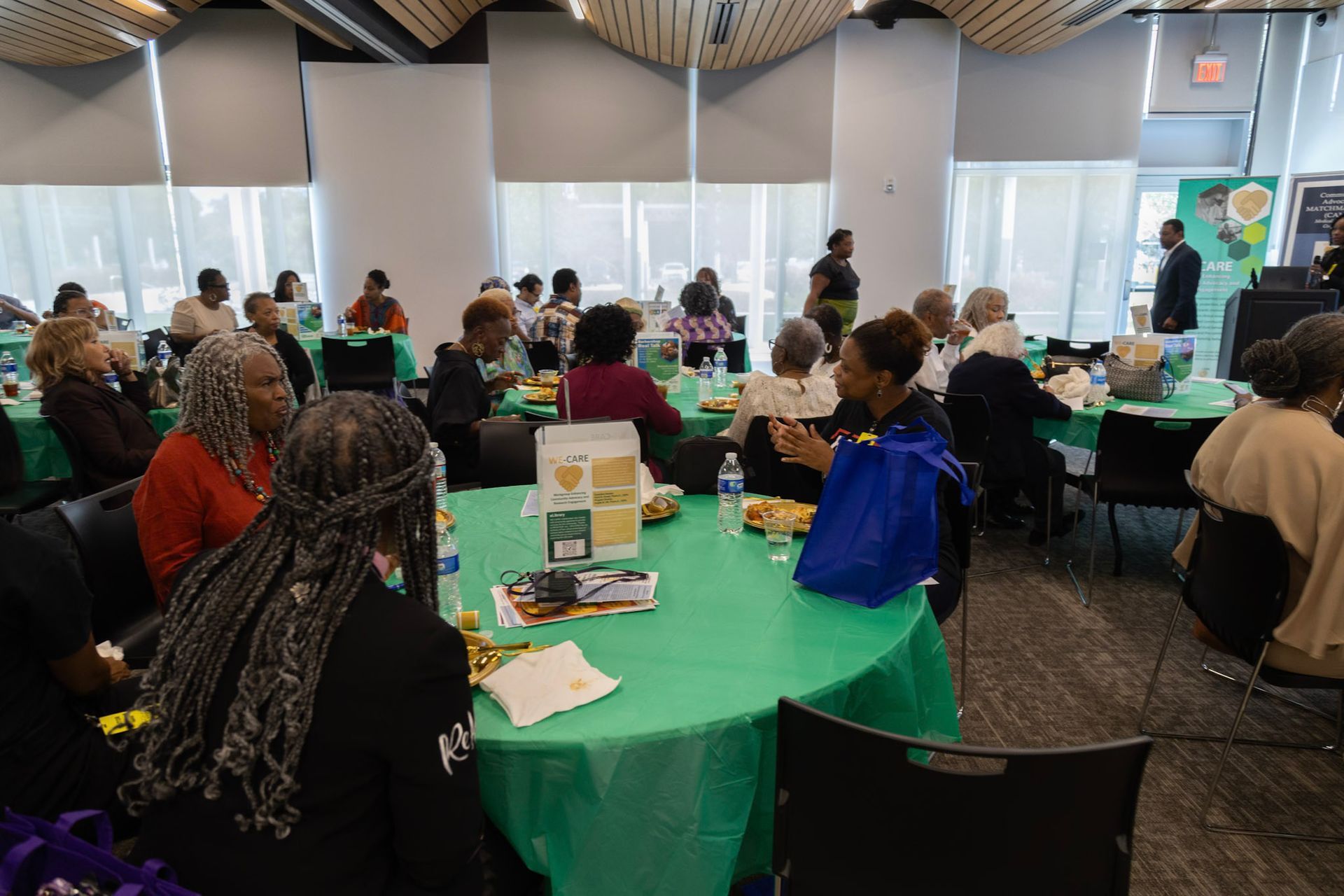 People seated at round green tables, gathered in a brightly lit room.