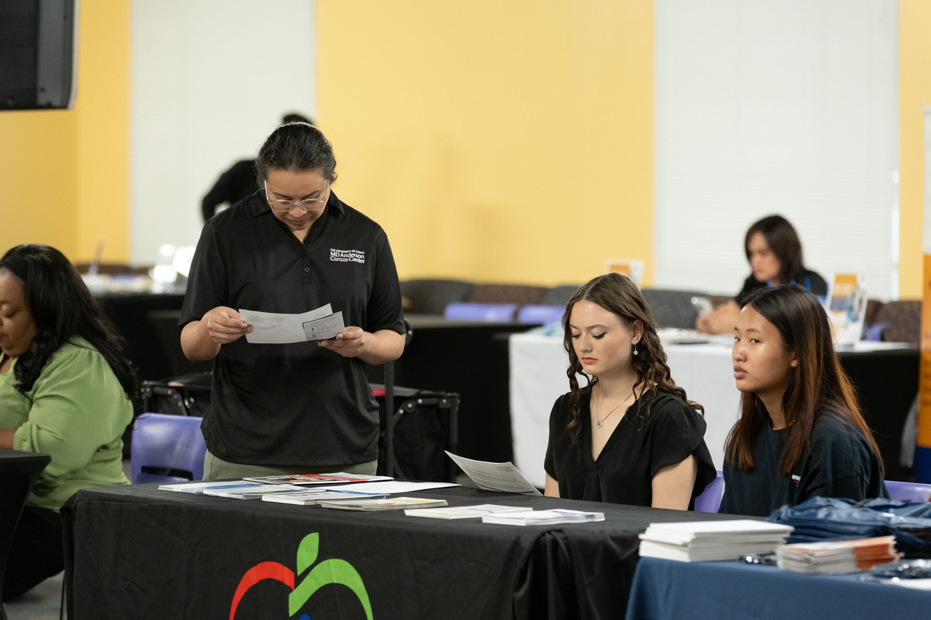 A woman reviews papers at a table with two other women at a career fair.