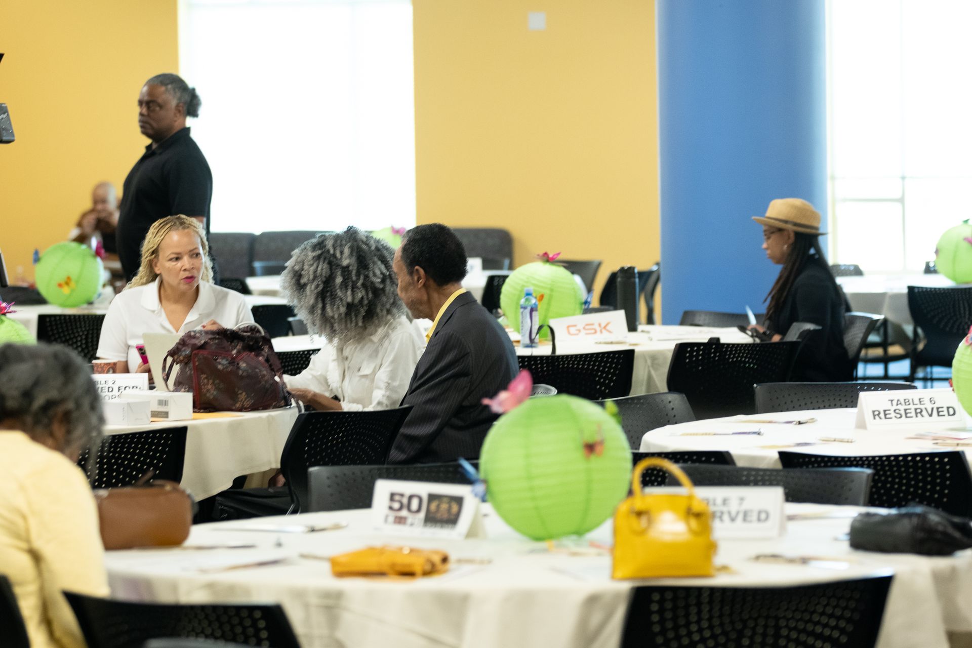 People seated at tables in a conference room, round tables with reserved signs and green paper lanterns.