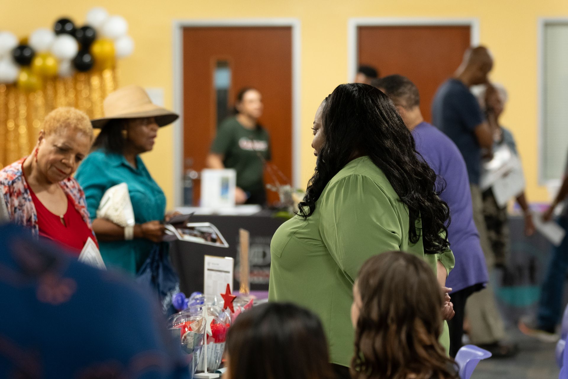 People attending an event at tables, including someone in green and an older woman looking down.