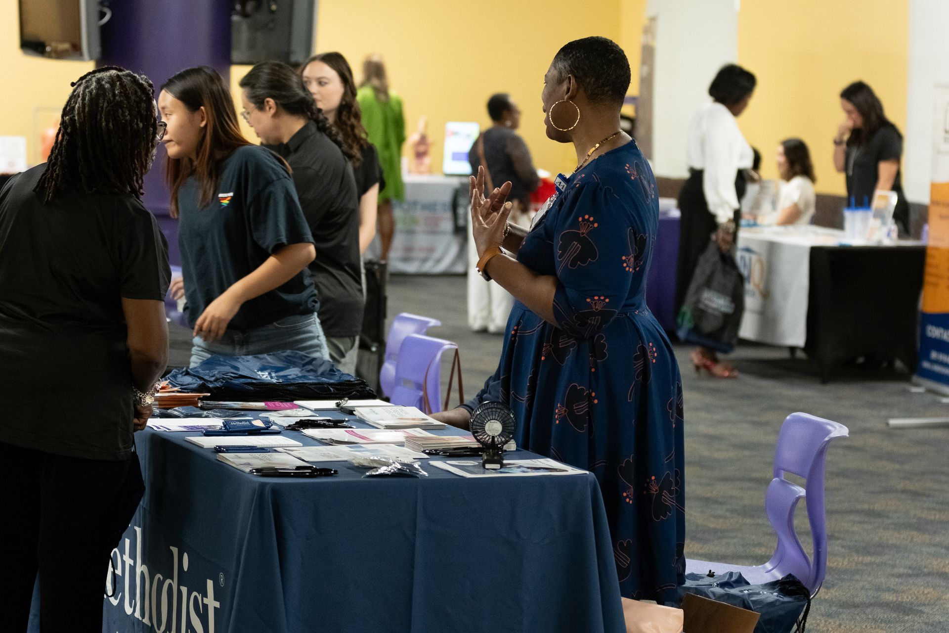 Career fair with people at tables, talking. Dark blue table cloth with 