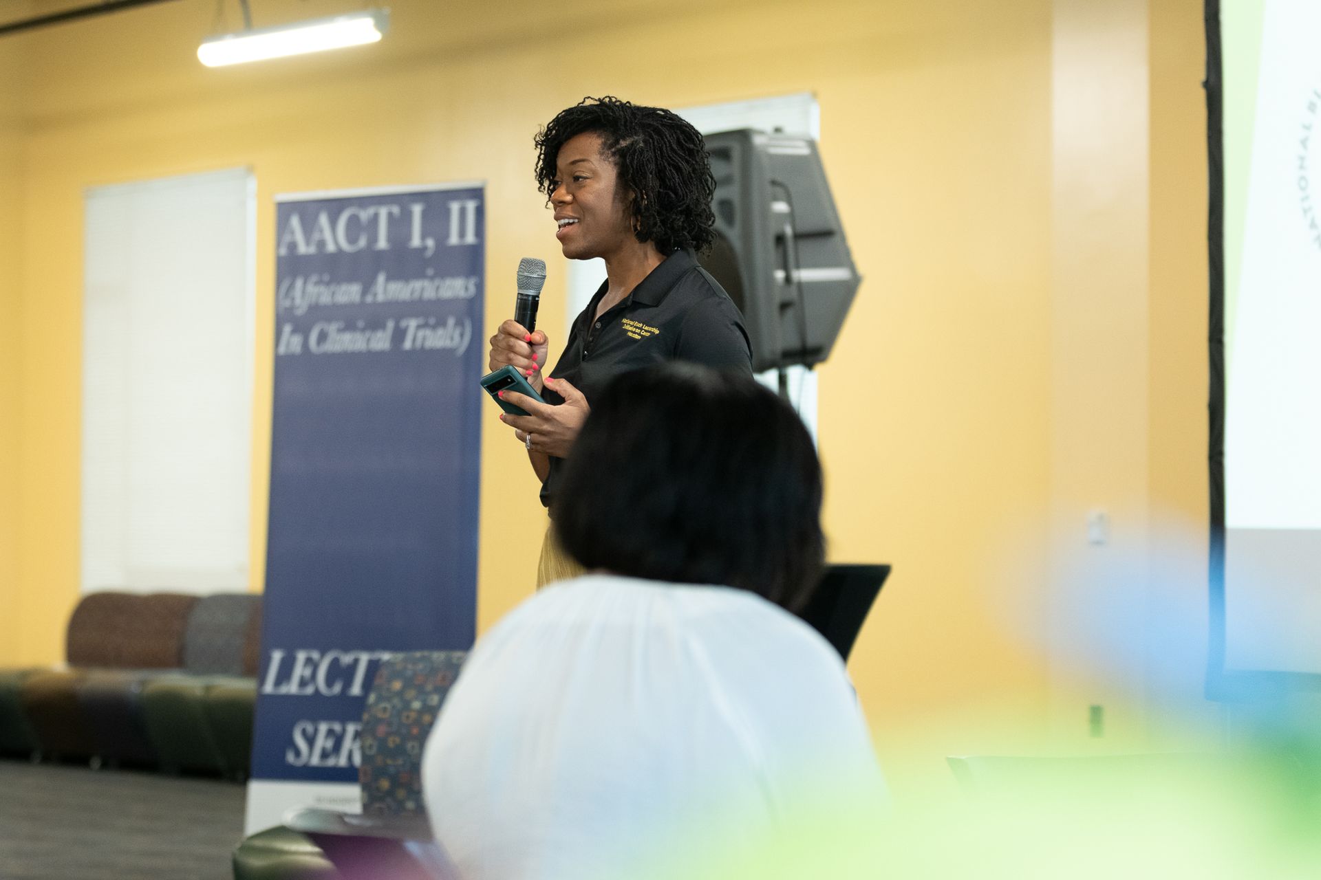 Woman speaking into a microphone, in front of a banner 