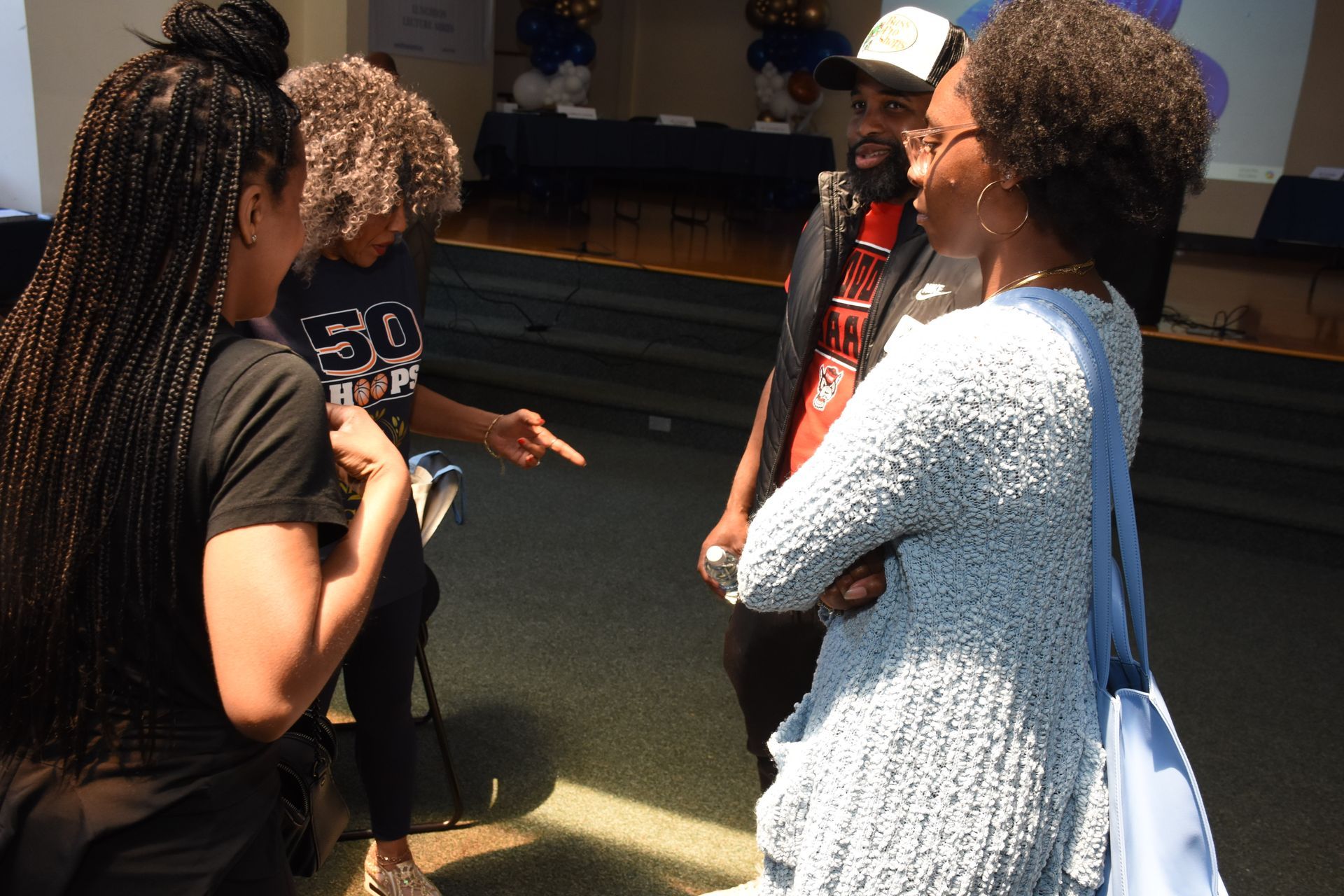 Four people in a room are in a conversation. One points, smiles, others look on. Blue and white decor.