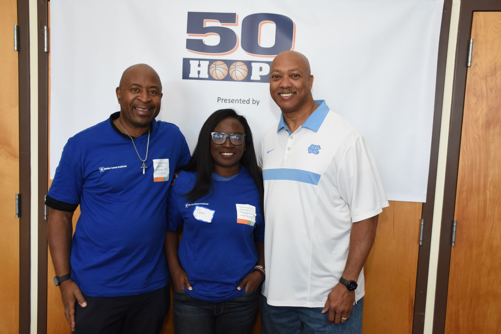 Three people in blue shirts stand in front of a banner that reads 